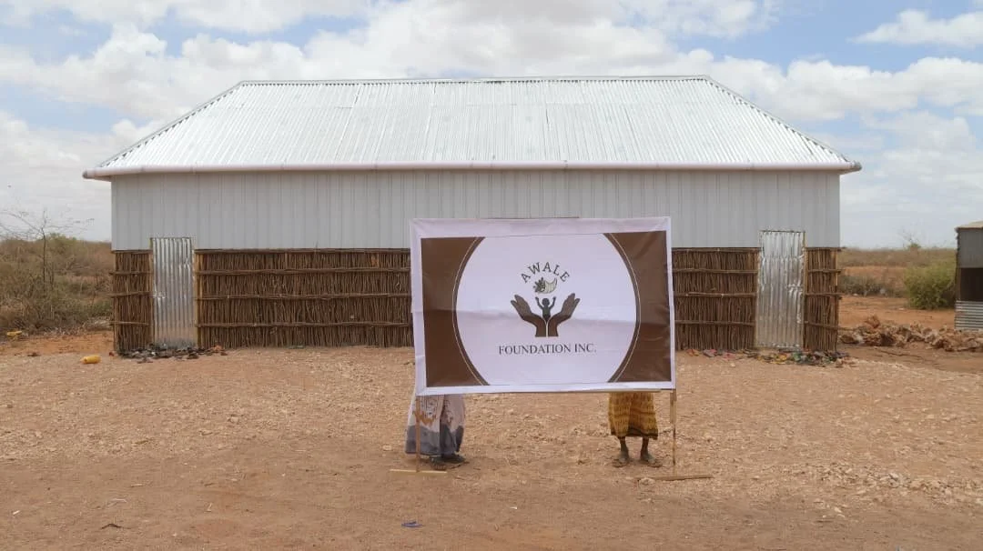 School built by Awale Foundation with Awale banner and two children in front of the building