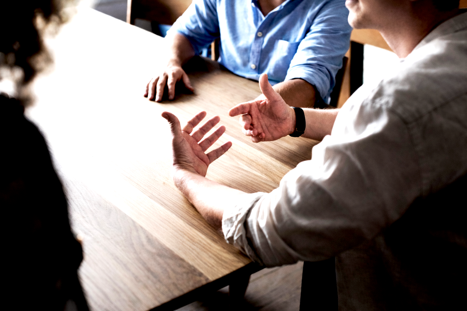 Mediation im Gespräch: Drei Personen sitzen an einem Tisch und klären einen beruflichen Konflikt, Gespräch zwischen Beteiligten an einem Besprechungstisch, Gesprächssituation in einer Mediation