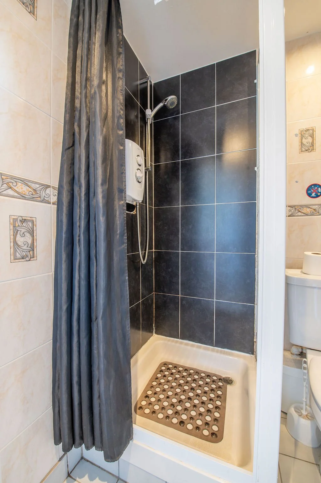 Small shower stall with black tiles, a gray shower curtain, shower head, and a bath console.
