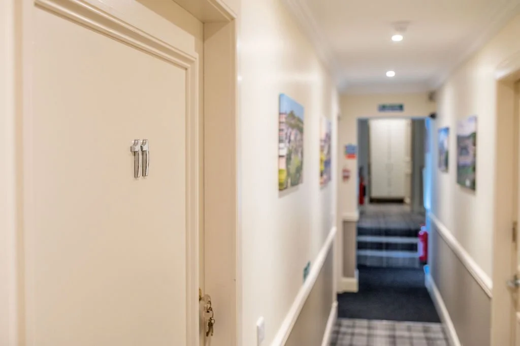Hallway with artwork on the walls, a small set of stairs at the end, and fire extinguishers near the staircase.