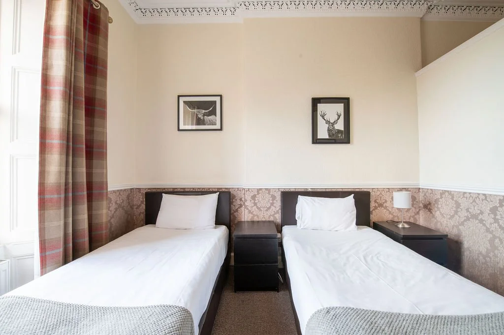 Hotel room with two single beds, dark wood headboards, twin nightstands, white bedding, and framed animal pictures on the wall.