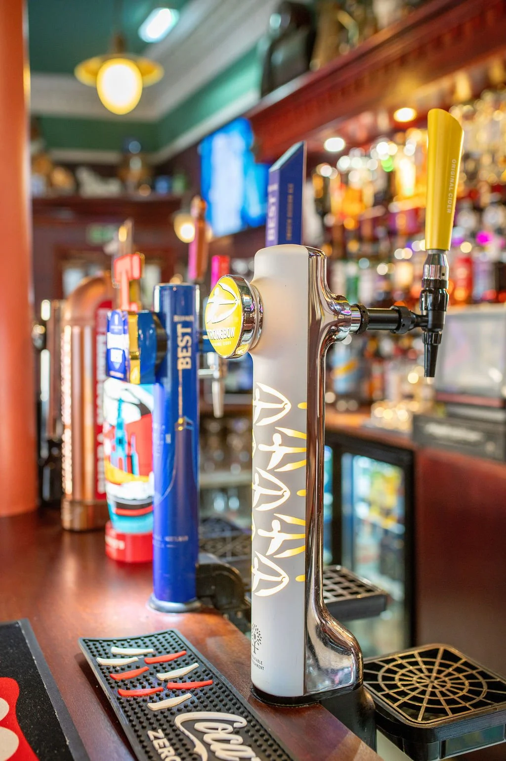 Beer tap handles on a bar counter, with a white key-shaped handle in the foreground and other colorful handles in the background.