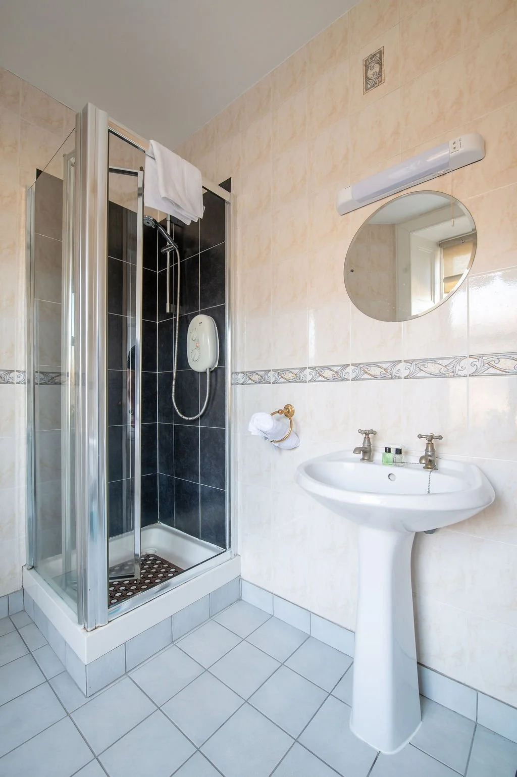 Bathroom with a shower stall, a pedestal sink, a mirror, and beige tiled walls.