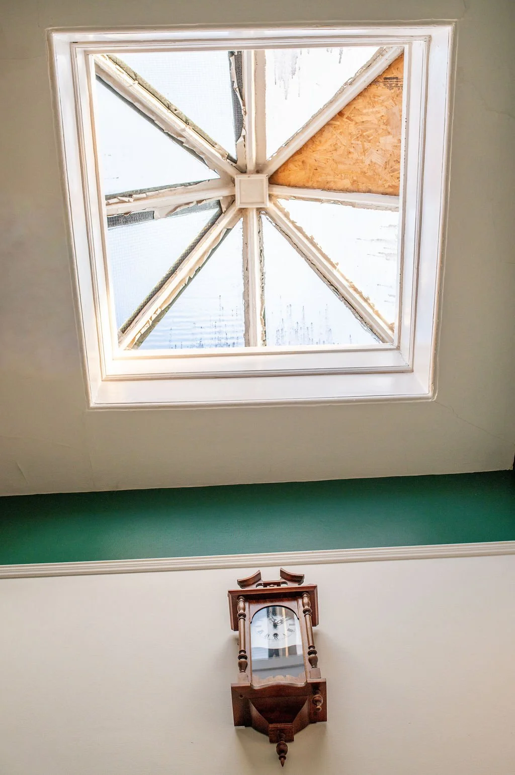 Ceiling with a decorative clock and a square skylight with visible wooden framing and construction materials.