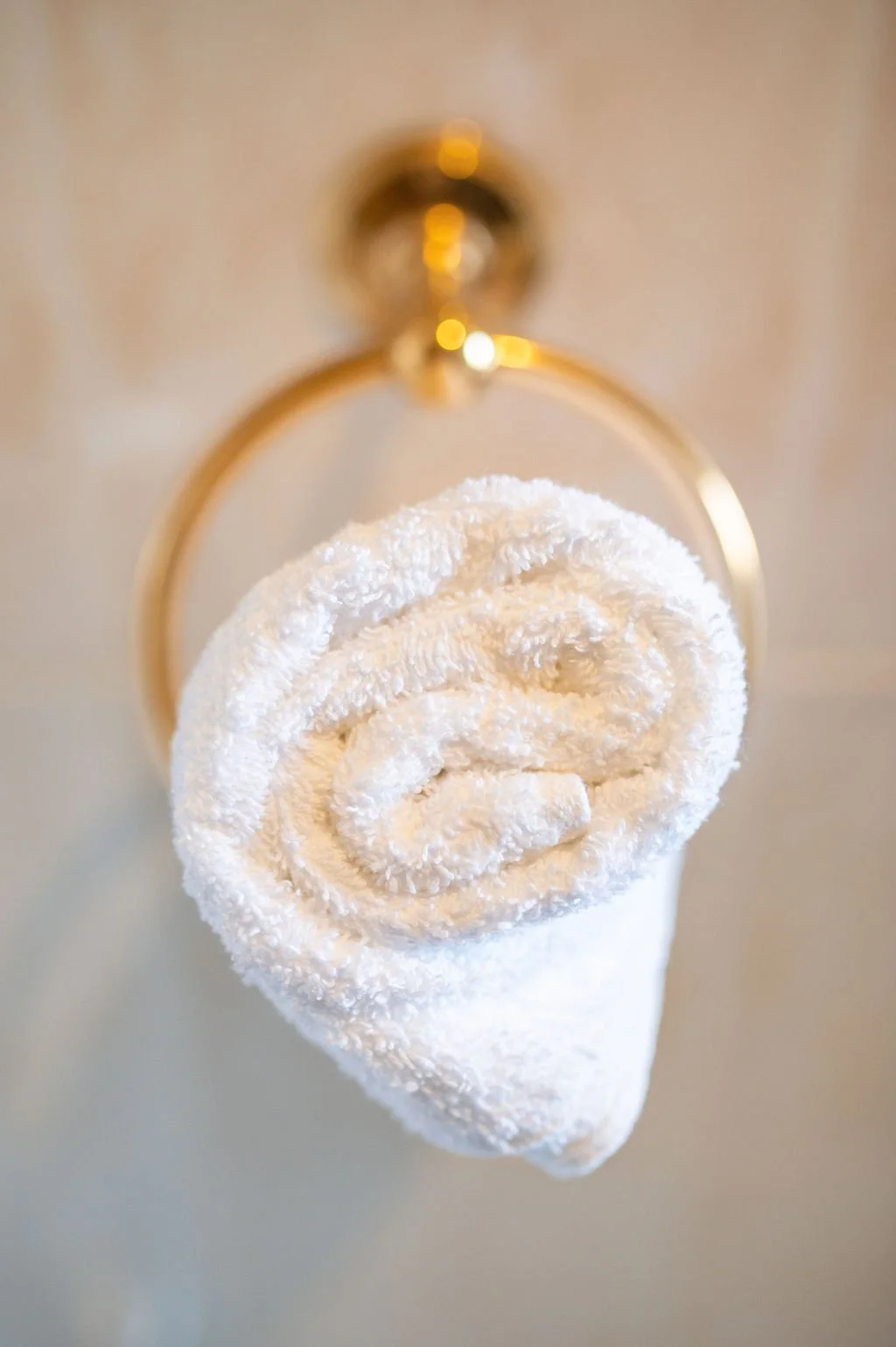 A neatly rolled white towel hanging on a gold towel ring attached to a wall.