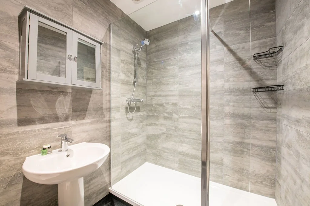 A modern bathroom with a walk-in shower, a small wall-mounted cabinet, and a pedestal sink.
