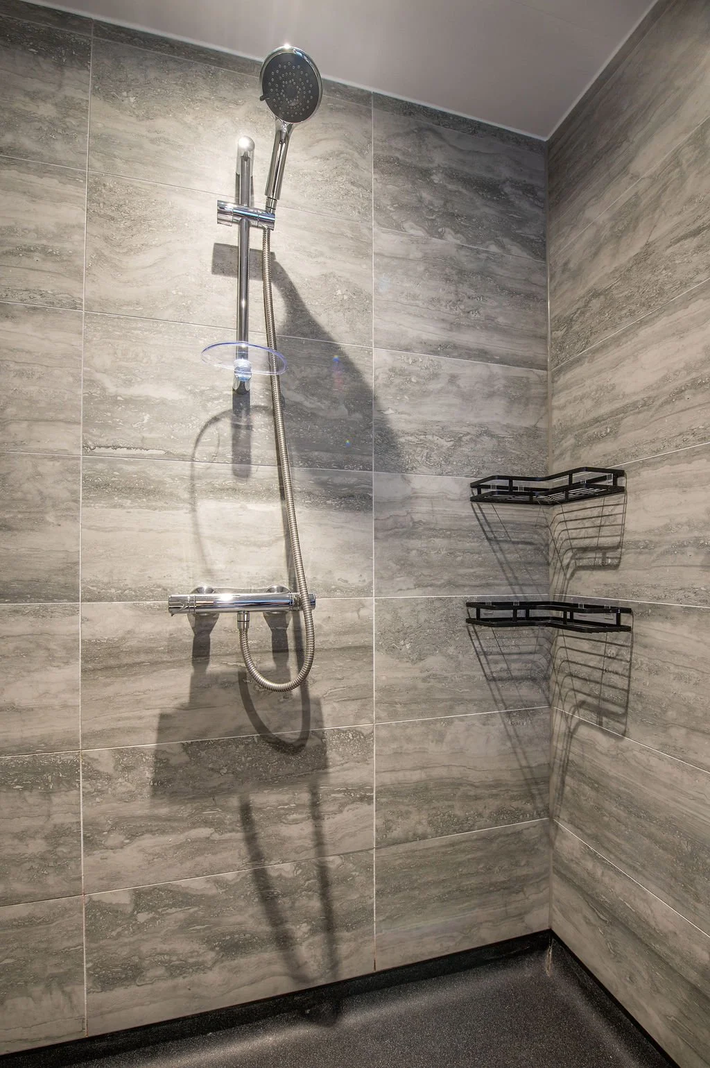 Shower head and shelf in a modern bathroom shower with gray tile walls.