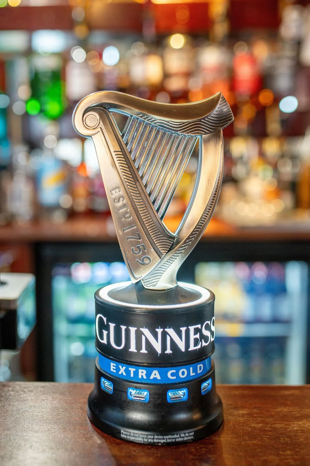 Guinness extra cold beer tap trophy with a harp design, placed on a bar counter with a blurred bar background.