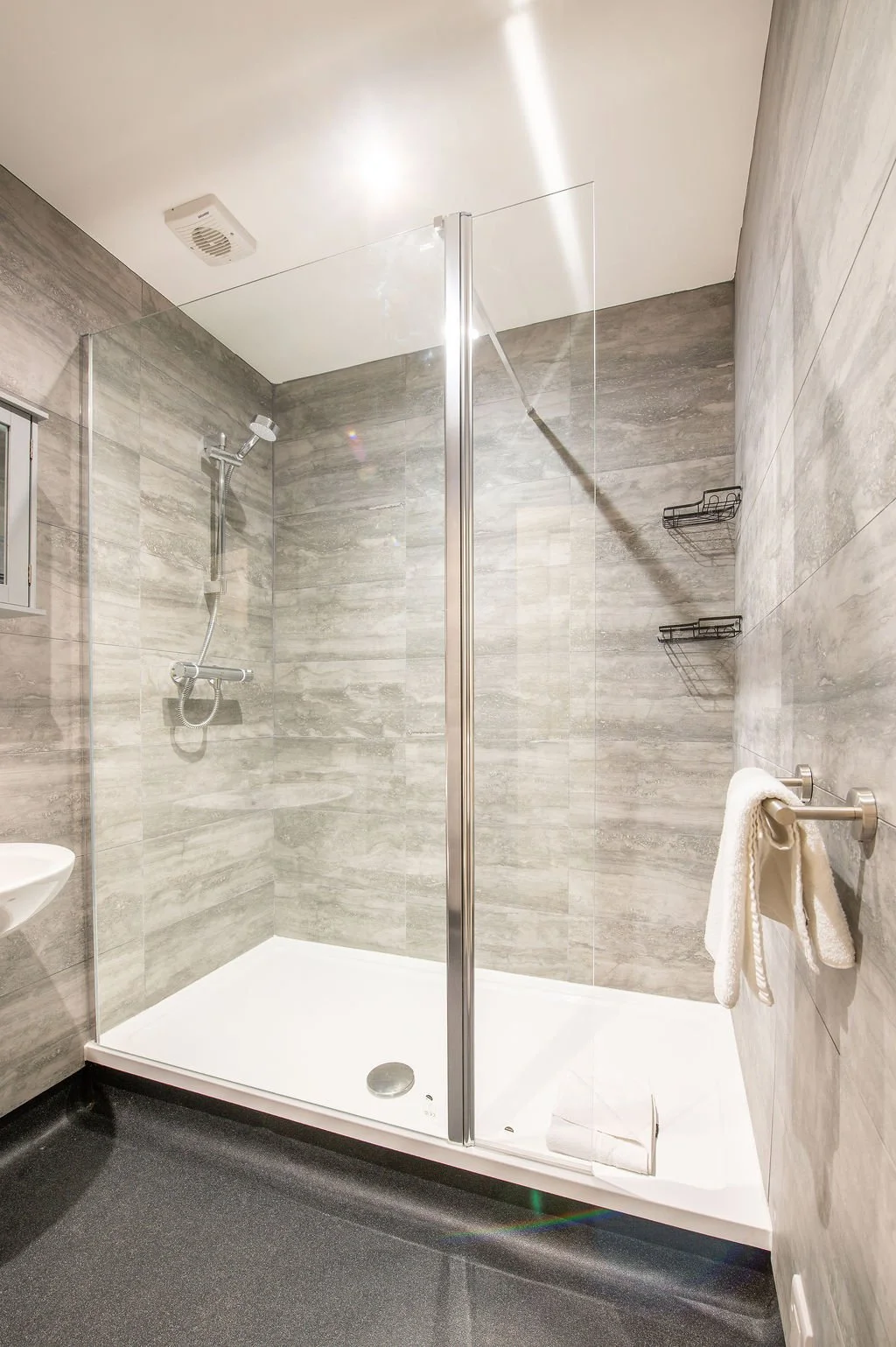 Photo of a modern shower with gray tiles, a glass door, and mounted shower fixtures.