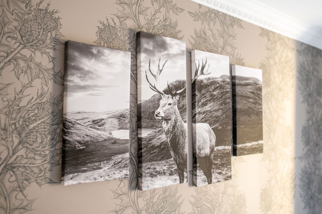 Black and white multi-panel canvas artwork of a stag in a mountainous landscape with a lake, hung on a wallpapered wall.