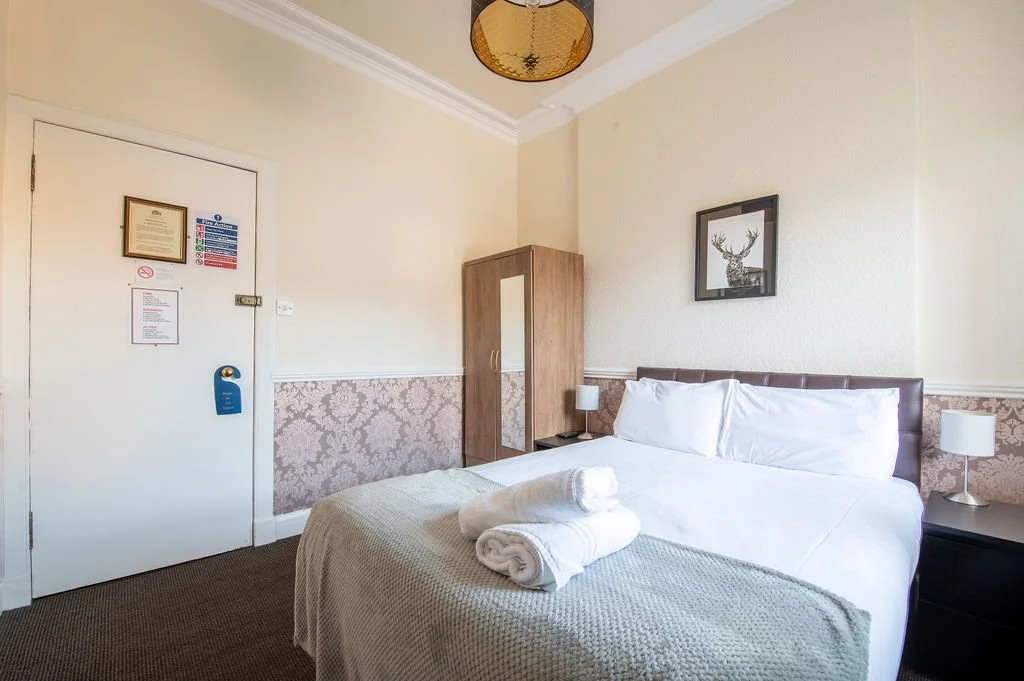 Clean hotel room with a bed, nightstands, lamps, a wardrobe, and a framed deer picture on the wall.