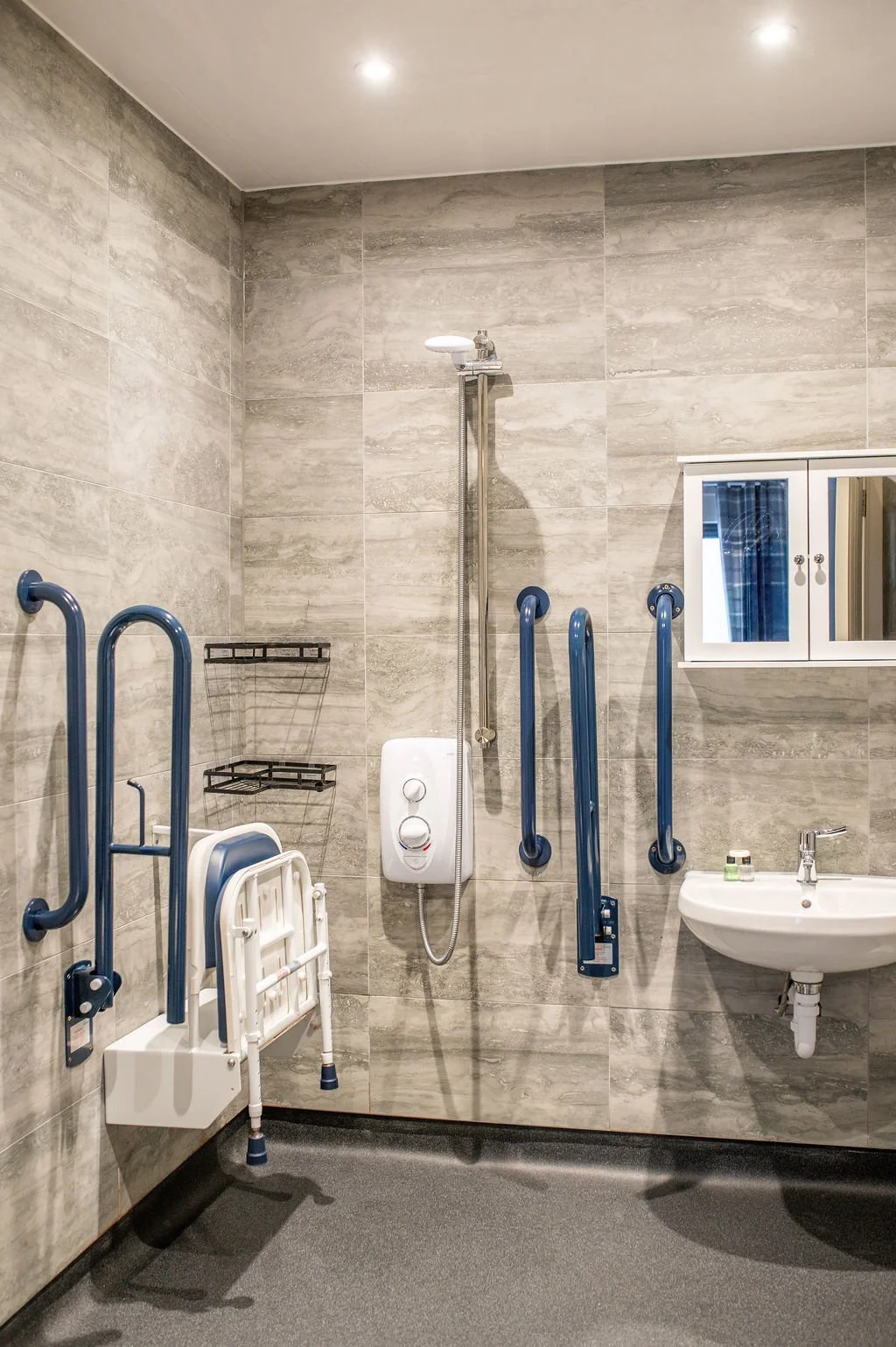Accessible shower with grab bars, foldable shower seat, and a sink with a mirror cabinet.