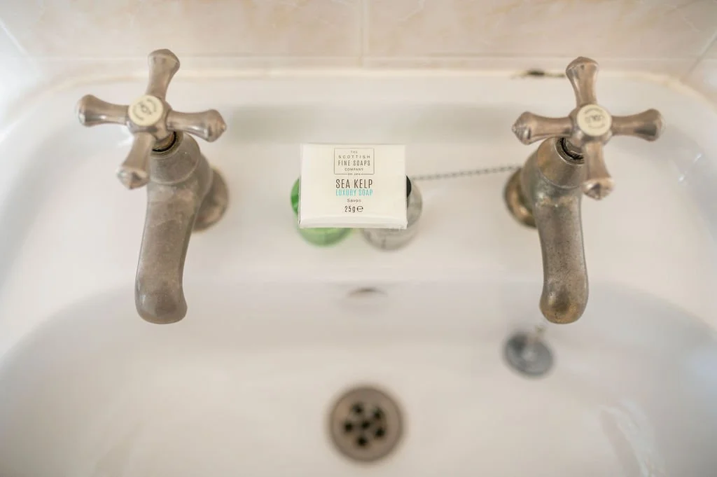 A bathroom sink with old, tarnished silver faucets and a bar of soap in the middle.