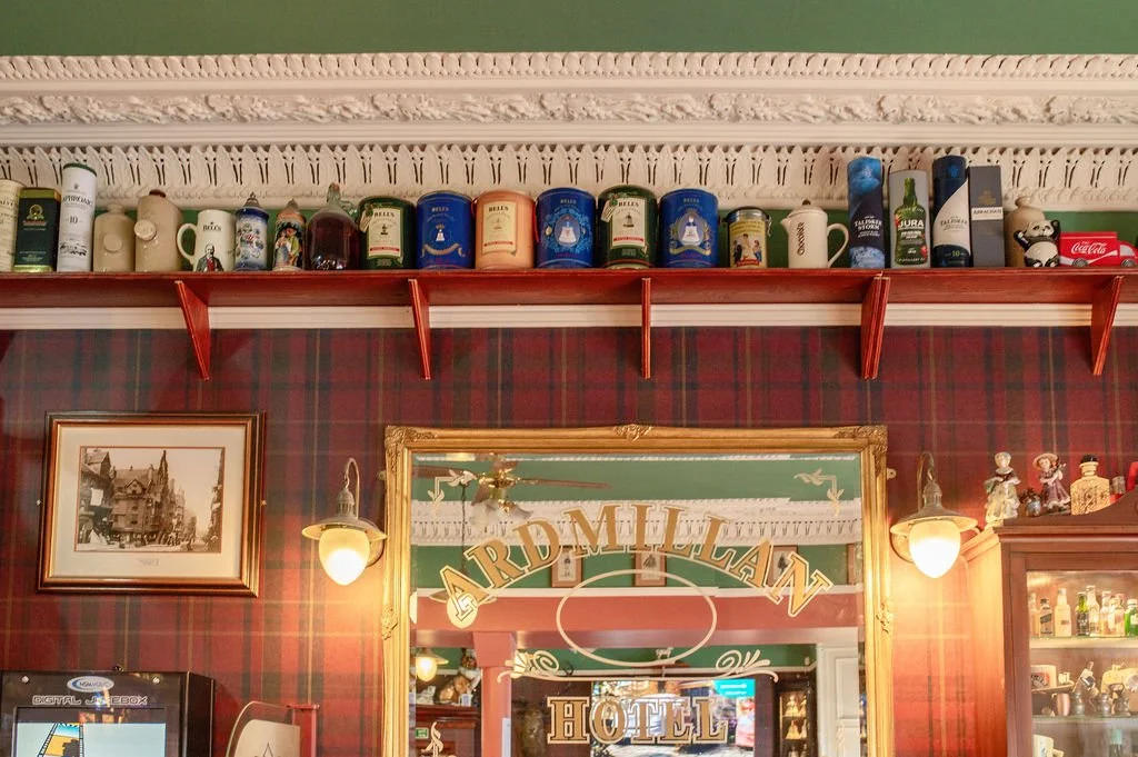Shelf with beer steins and bottles above a mirror in a hotel lobby with red plaid wallpaper and framed picture