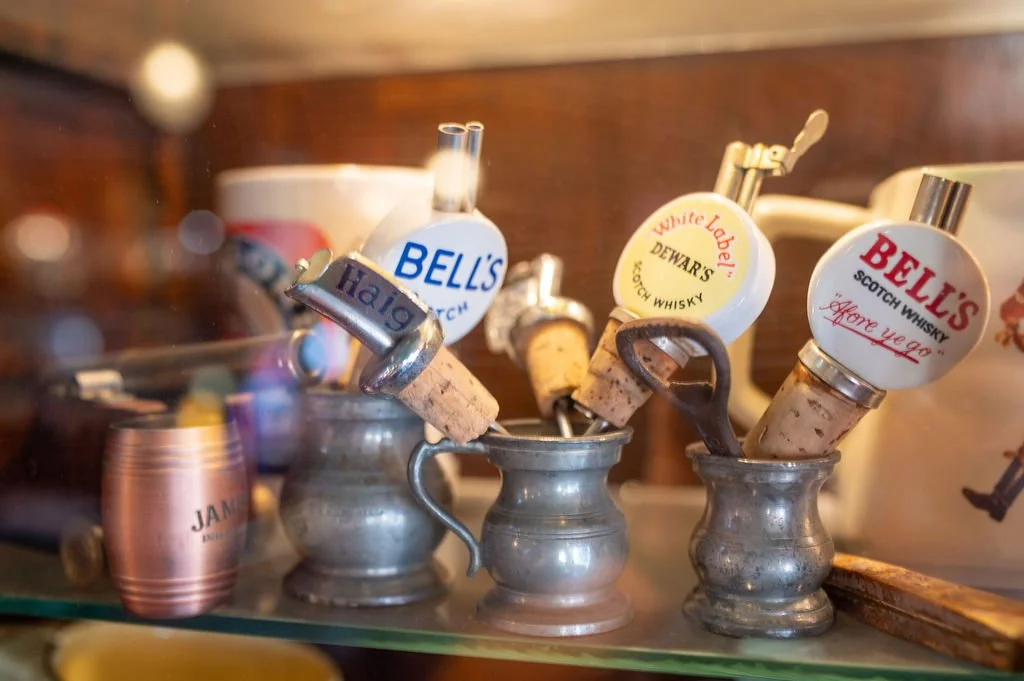 Close-up of metal cups with whiskey bottle caps and corks used as ornaments or dispensers on a glass surface.