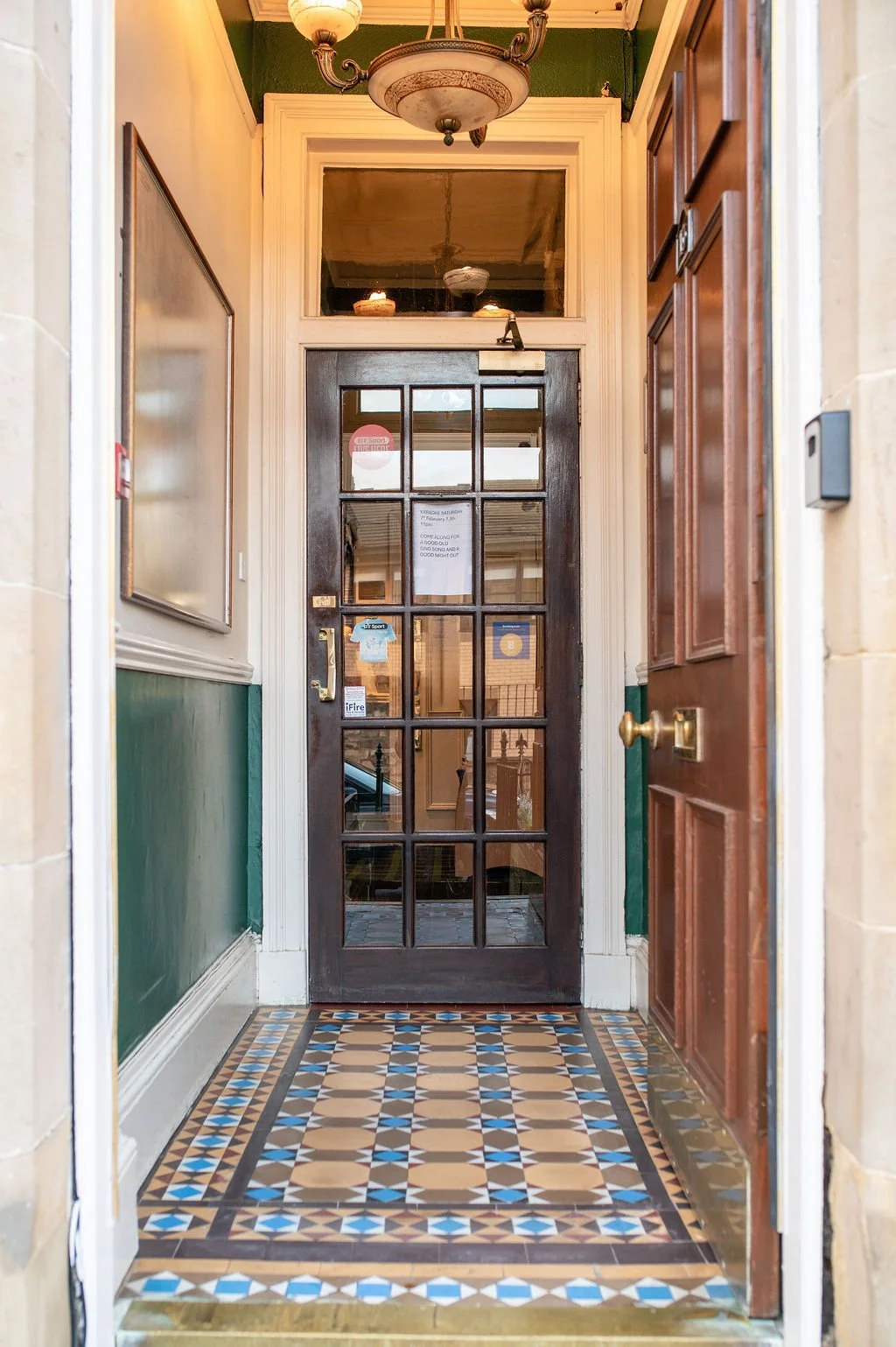 Inside view of a doorway with a glass-paneled wooden door, decorative tile floor, and an ornate ceiling light fixture.