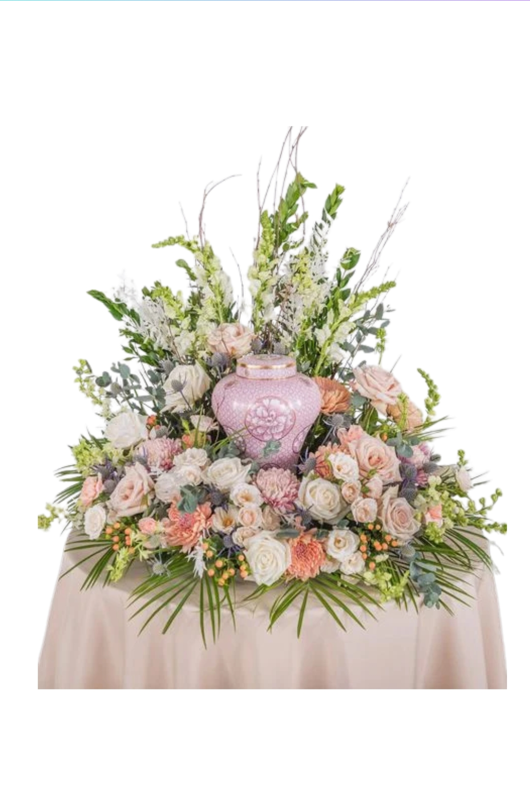 A floral arrangement with pink roses, white flowers, and greenery surrounding a pink decorative vase on a table with a beige tablecloth.