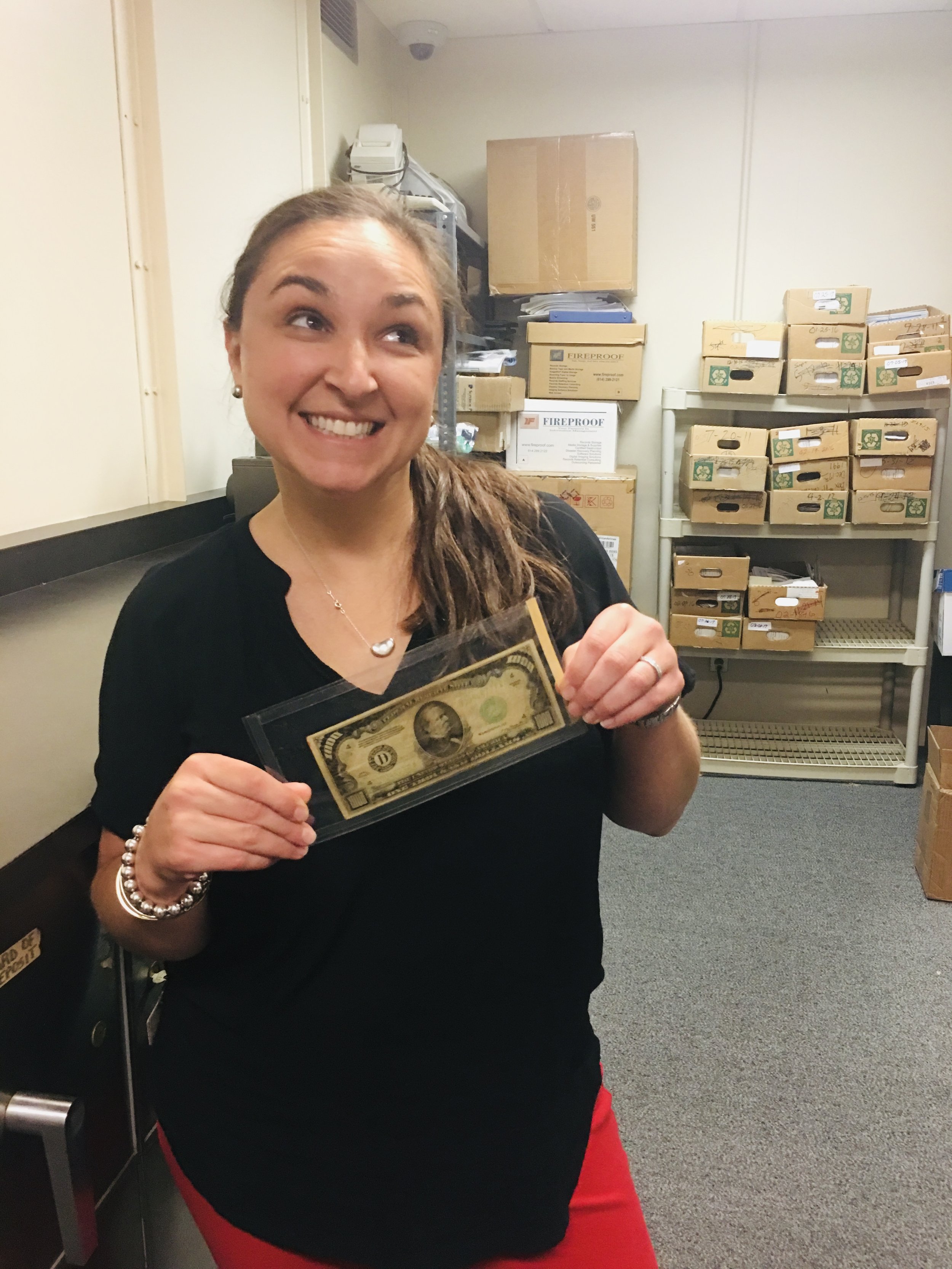 Tanya Hartman holding a hundred-dollar bill in a storage room for a nonprofit foundation
