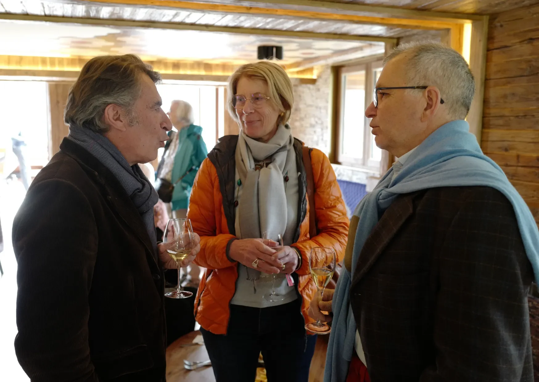 Trois personnes discutant lors d'un événement avec des verres de vin, dans une pièce en bois, décorée de manière chaleureuse.