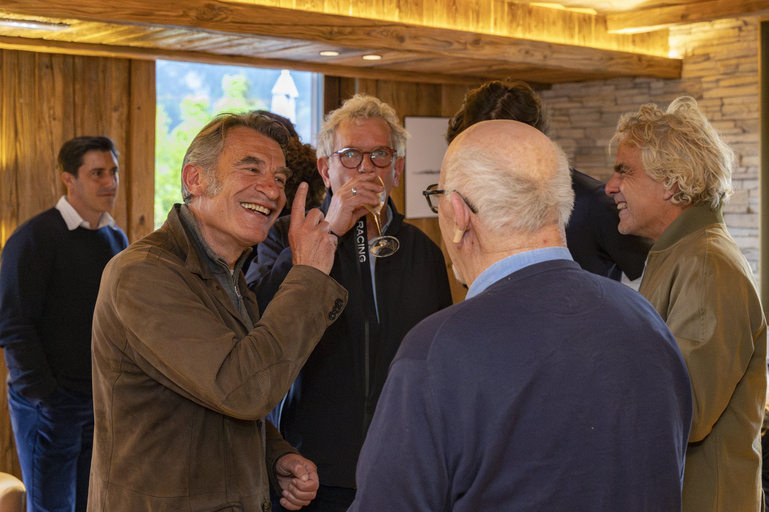 Groupe de personnes souriantes et discutant dans une pièce en bois, ambiance chaleureuse.