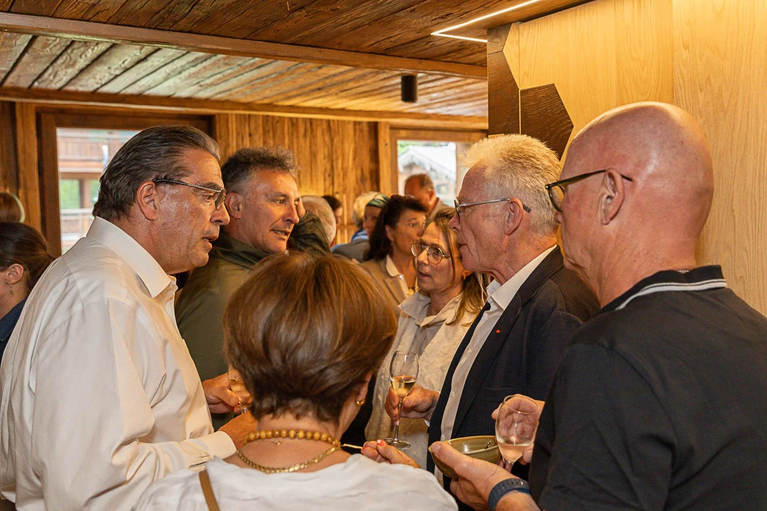 Groupe de personnes parlant et tenant des verres de vin lors d'une réunion ou d'une fête dans une pièce en bois