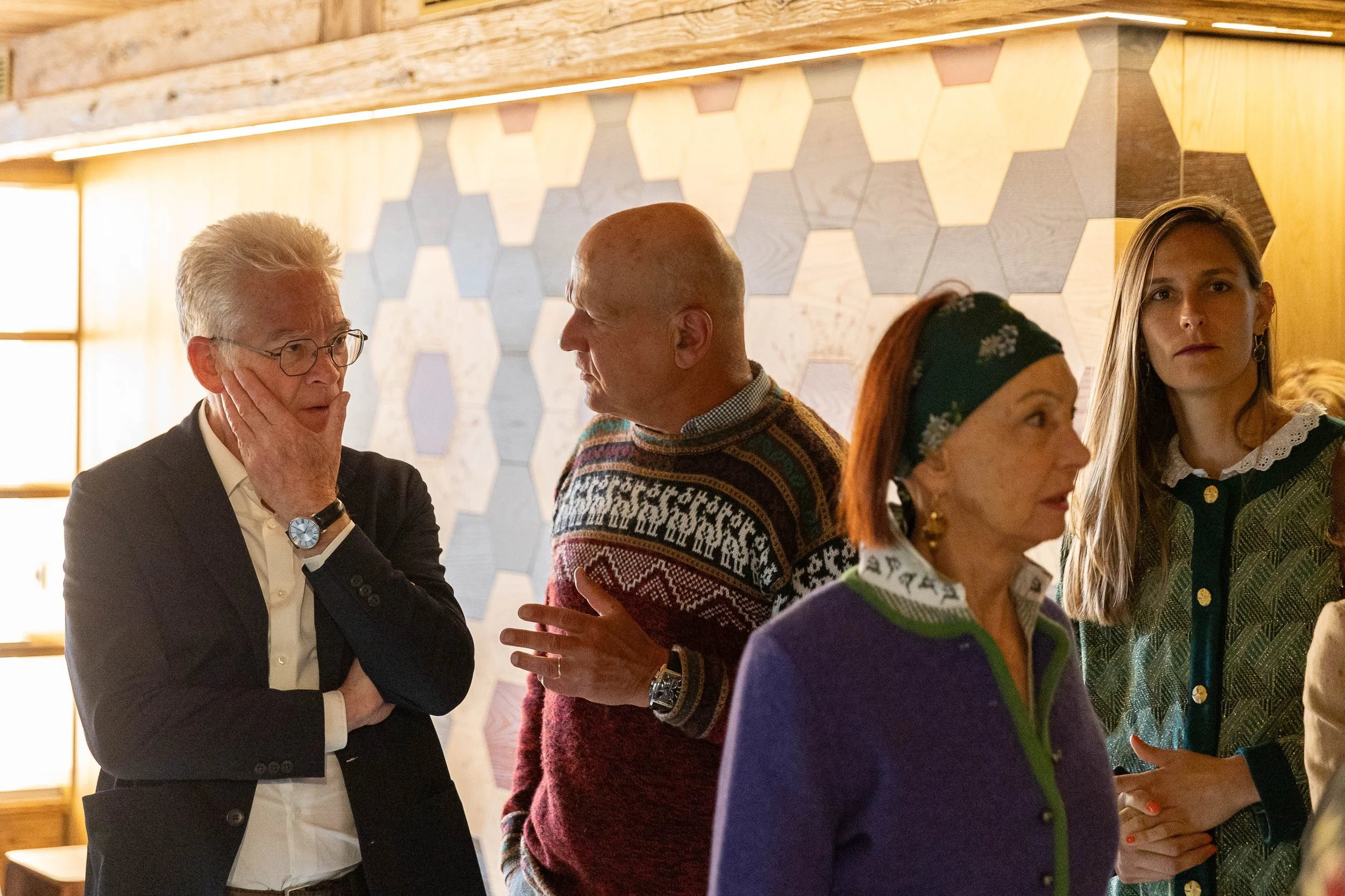 groupe de personnes discutant à l'intérieur avec un mur en bois et motifs hexagonaux en arrière-plan