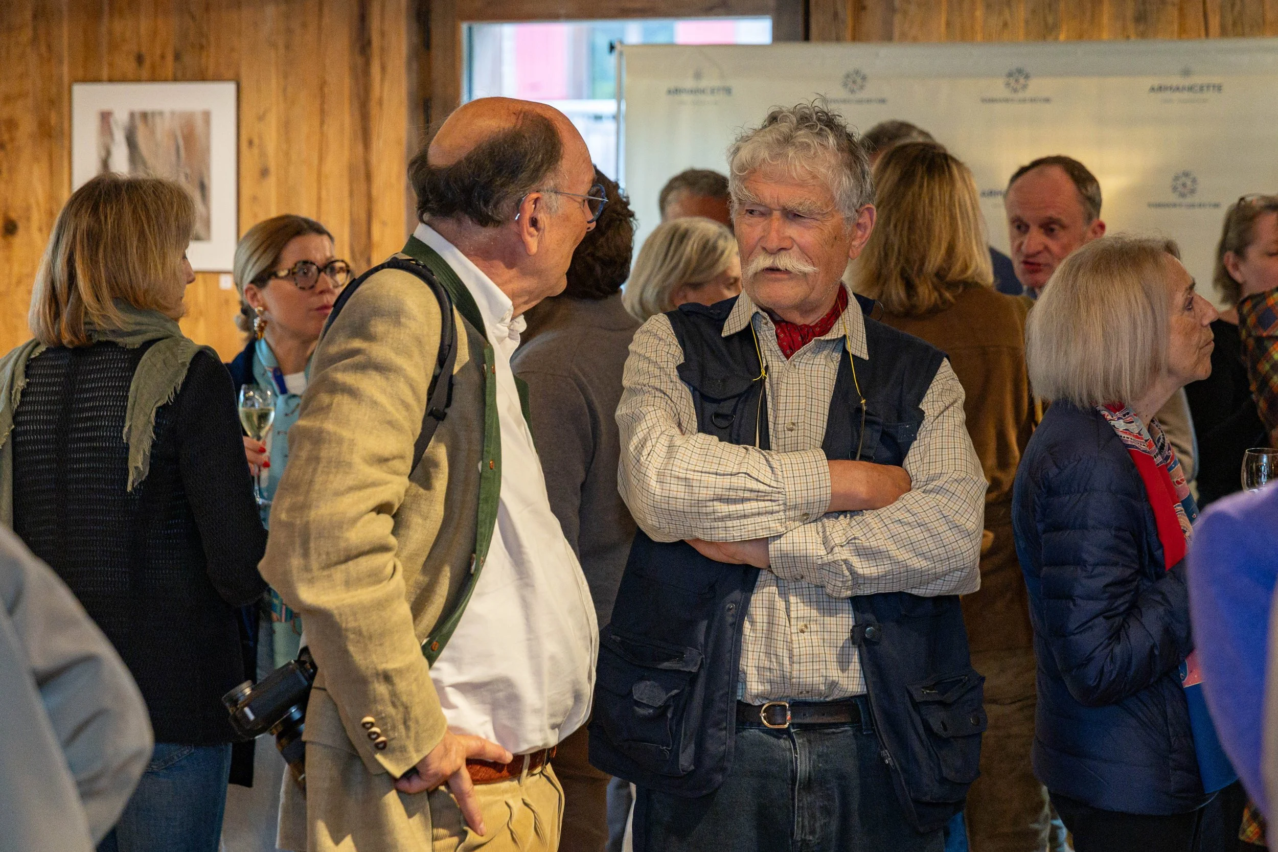 Groupe de personnes discutant lors d'un événement en intérieur, avec un mur en bois et une panneau d'affichage en arrière-plan.