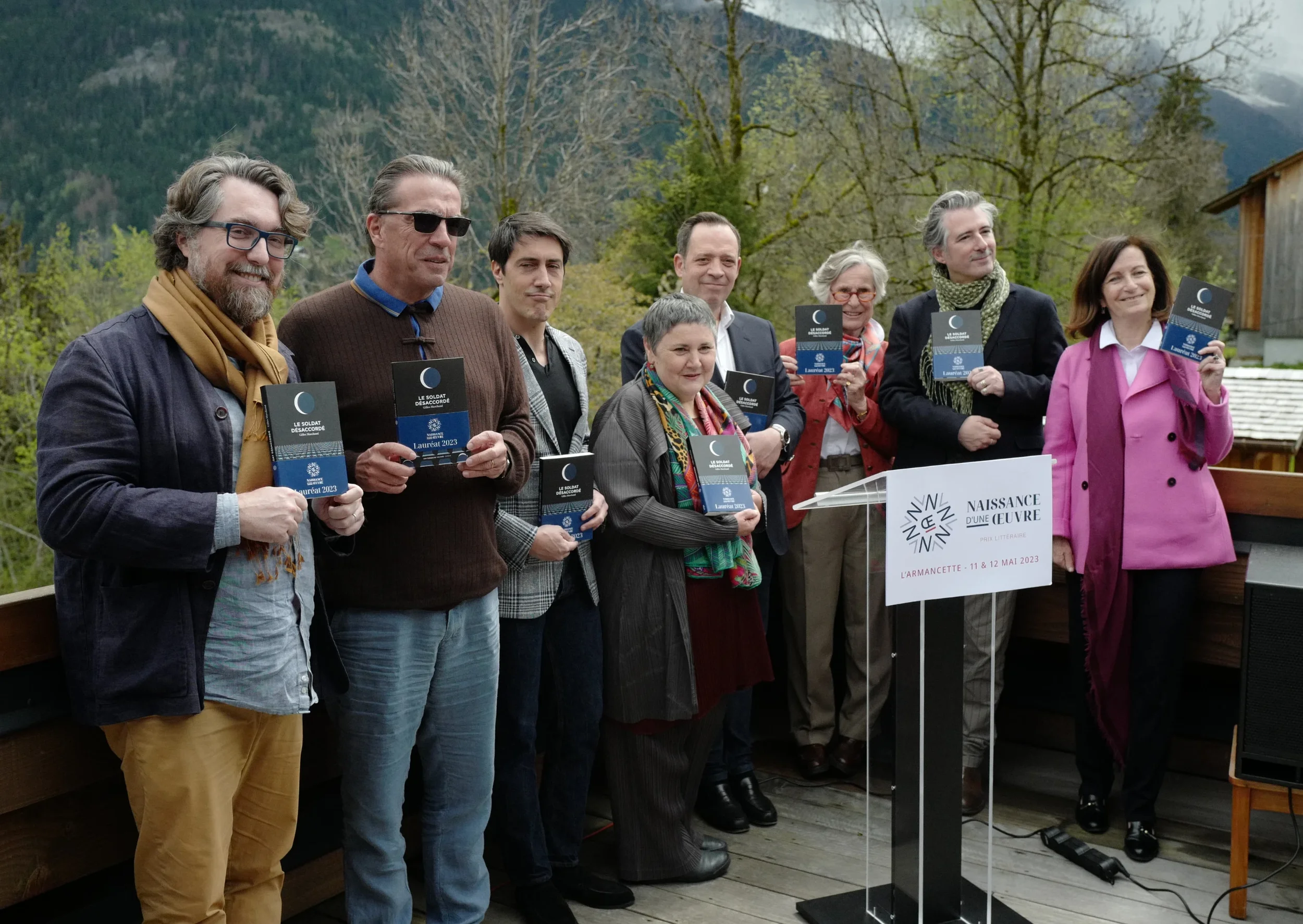 Groupe de personnes tenant des affiches à une cérémonie en plein air avec un paysage de montagnes en arrière-plan.