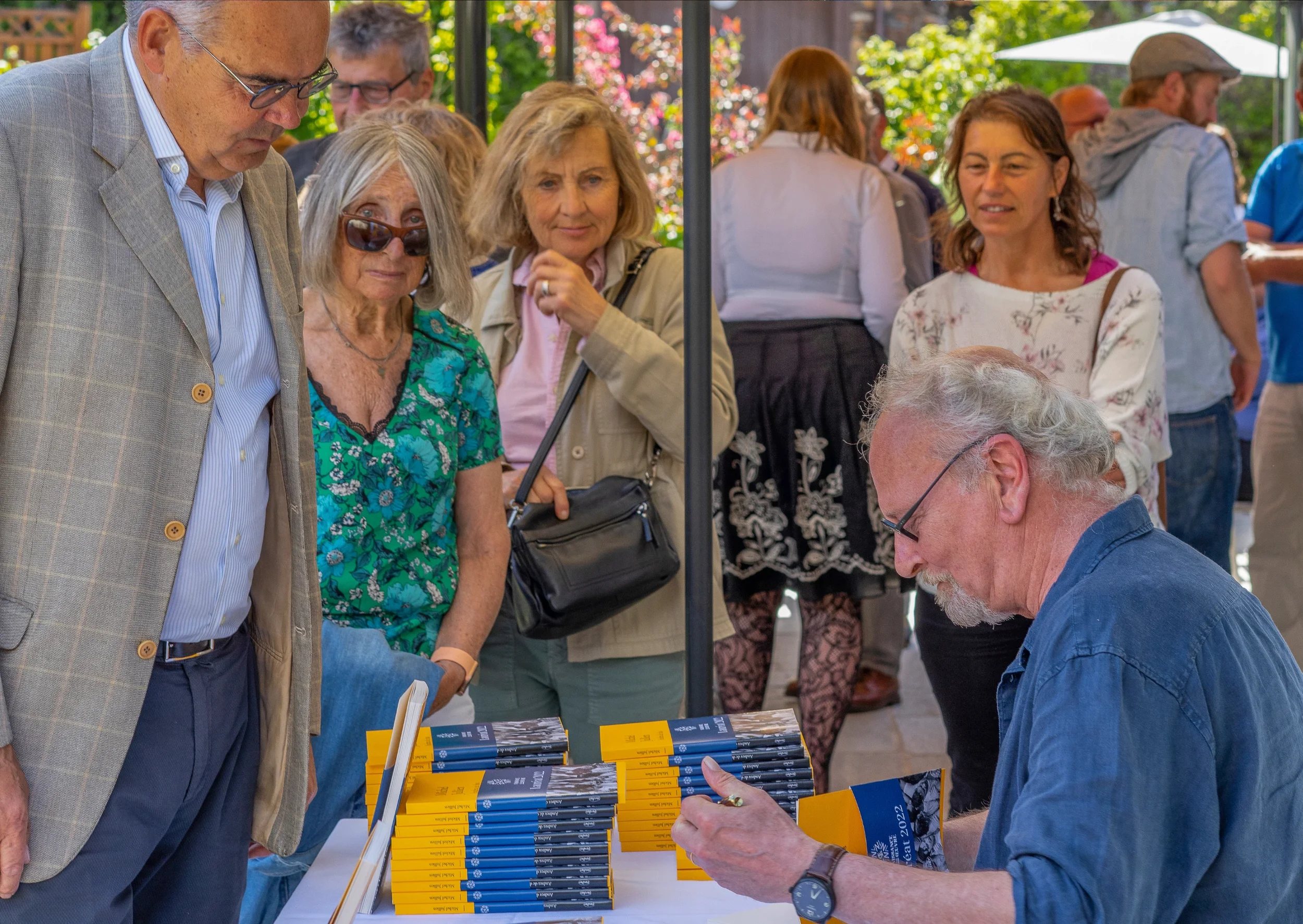 Groupe de personnes au stand de livres lors d'un événement en plein air, avec des participants regardant des livres sur la table.