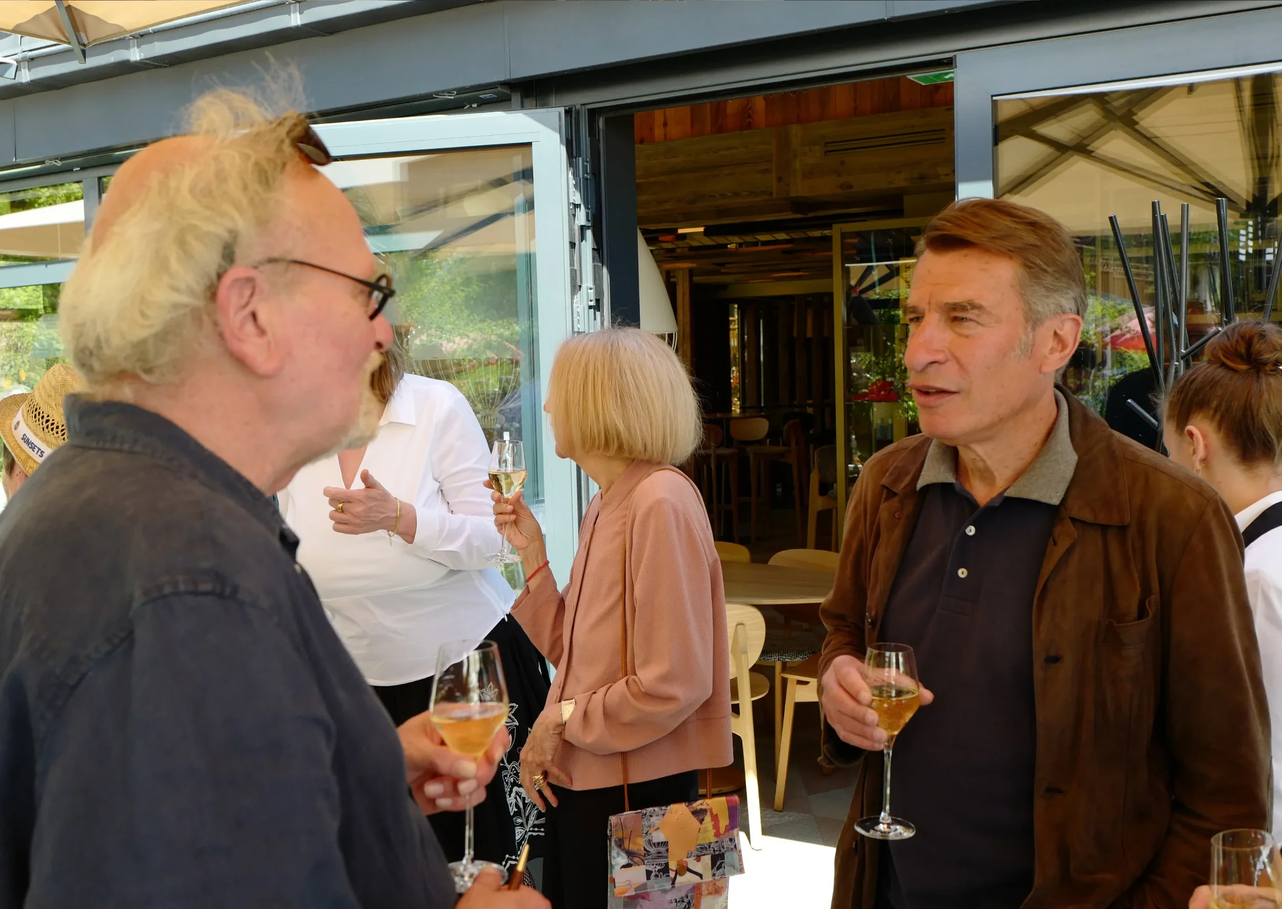 Groupe de personnes en conversation lors d'une réunion sociale à l'intérieur, avec des verres de vin ou de champagne.