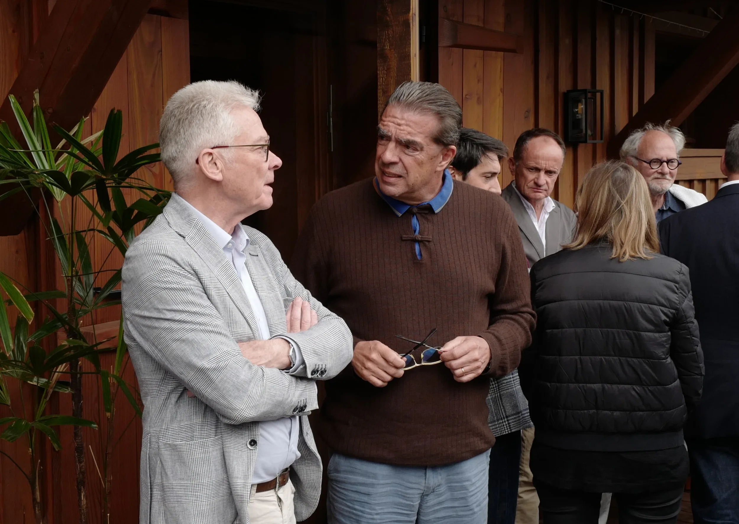 Groupe de personnes discutant lors d'un rassemblement, avec des murs en bois en arrière-plan.