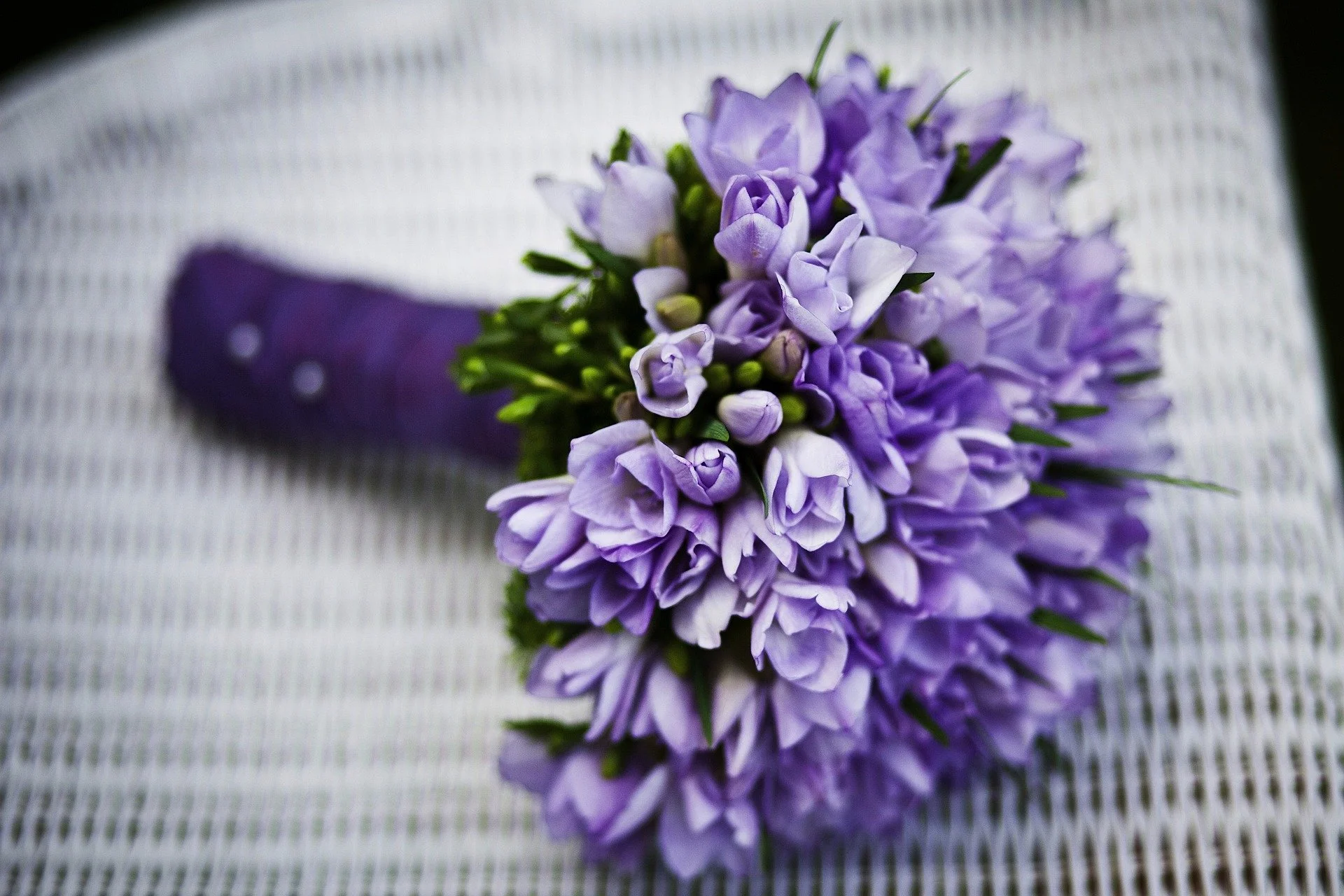 Close-up of a purple flower bouquet with green stems, placed on a textured white surface.