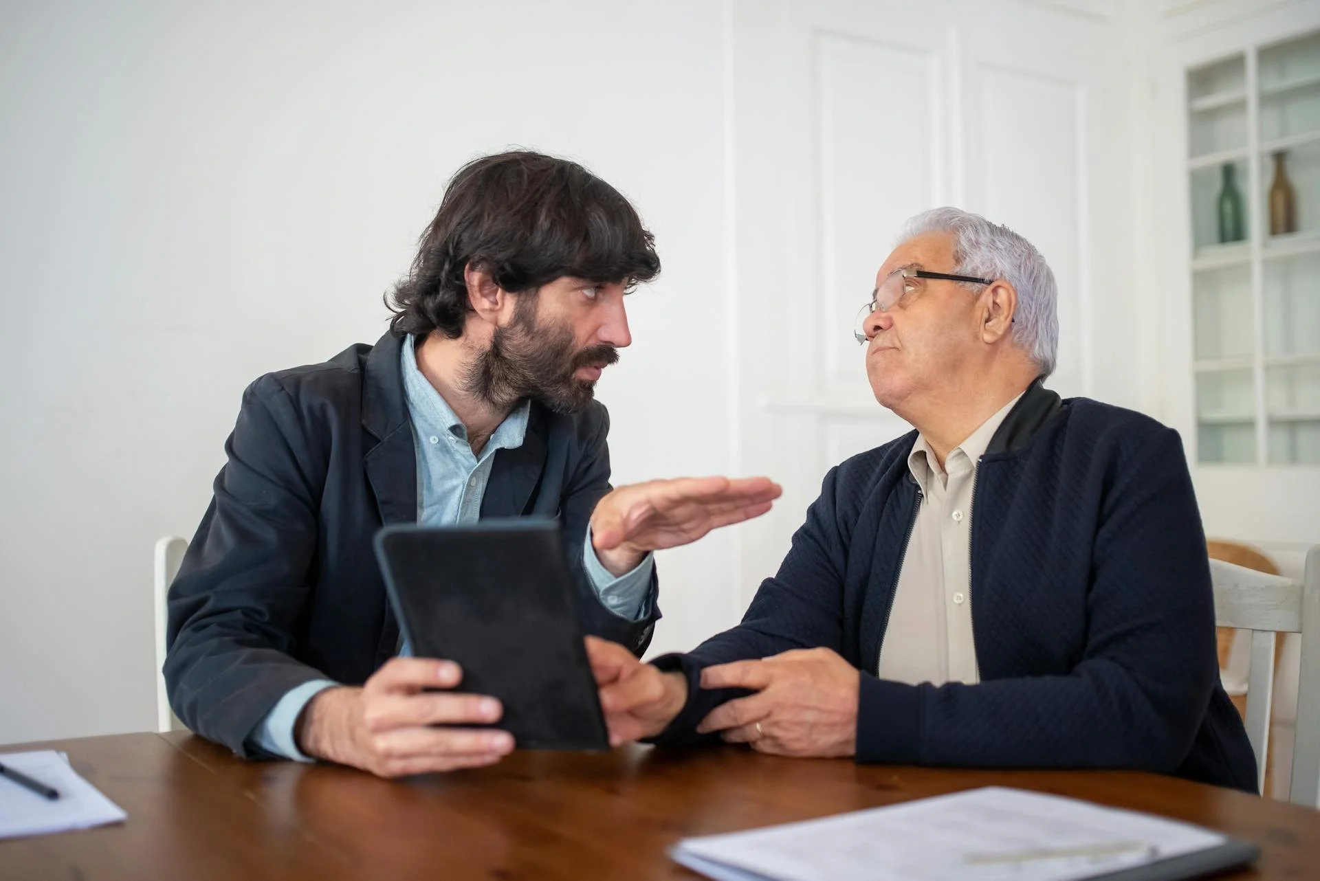 Deux hommes en discussion sérieuse à une table, l'un semble argumenter, l'autre écoute attentivement