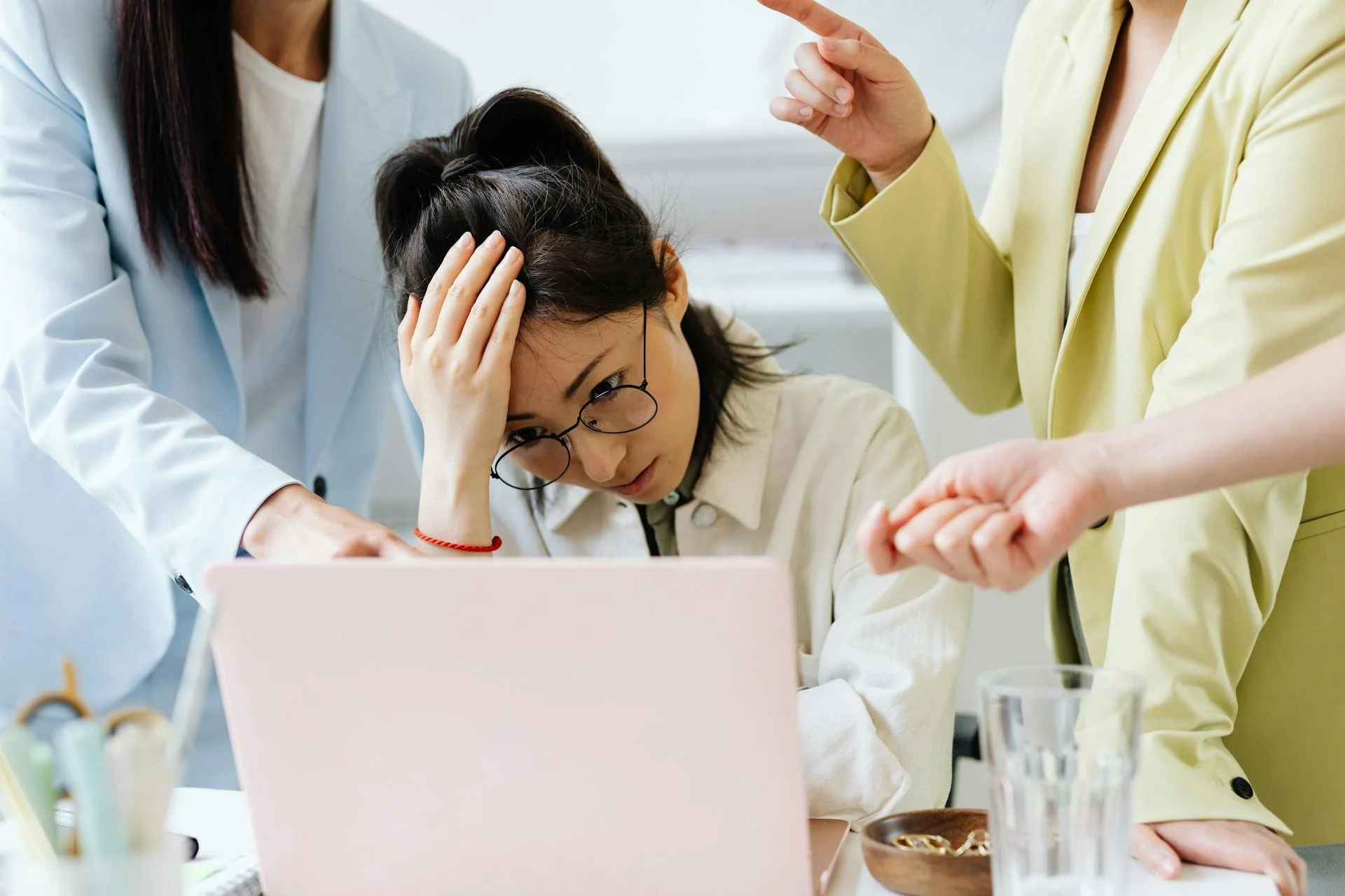 Une femme semble stressée ou frustrée, avec une main sur la tête, entourée de plusieurs personnes en discussion.