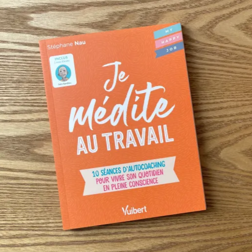 Livre orange intitulé "Je médite au travail" de Stéphane Nau coach et formateur posé sur une table en bois