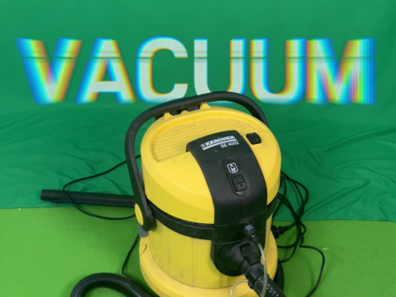 Ein gelber Staubsauger mit schwarzen Griff und Kabel vor einem grünen Hintergrund, auf dem das Wort 'VACUUM' in bunten, verzerrten Buchstaben angezeigt wird.