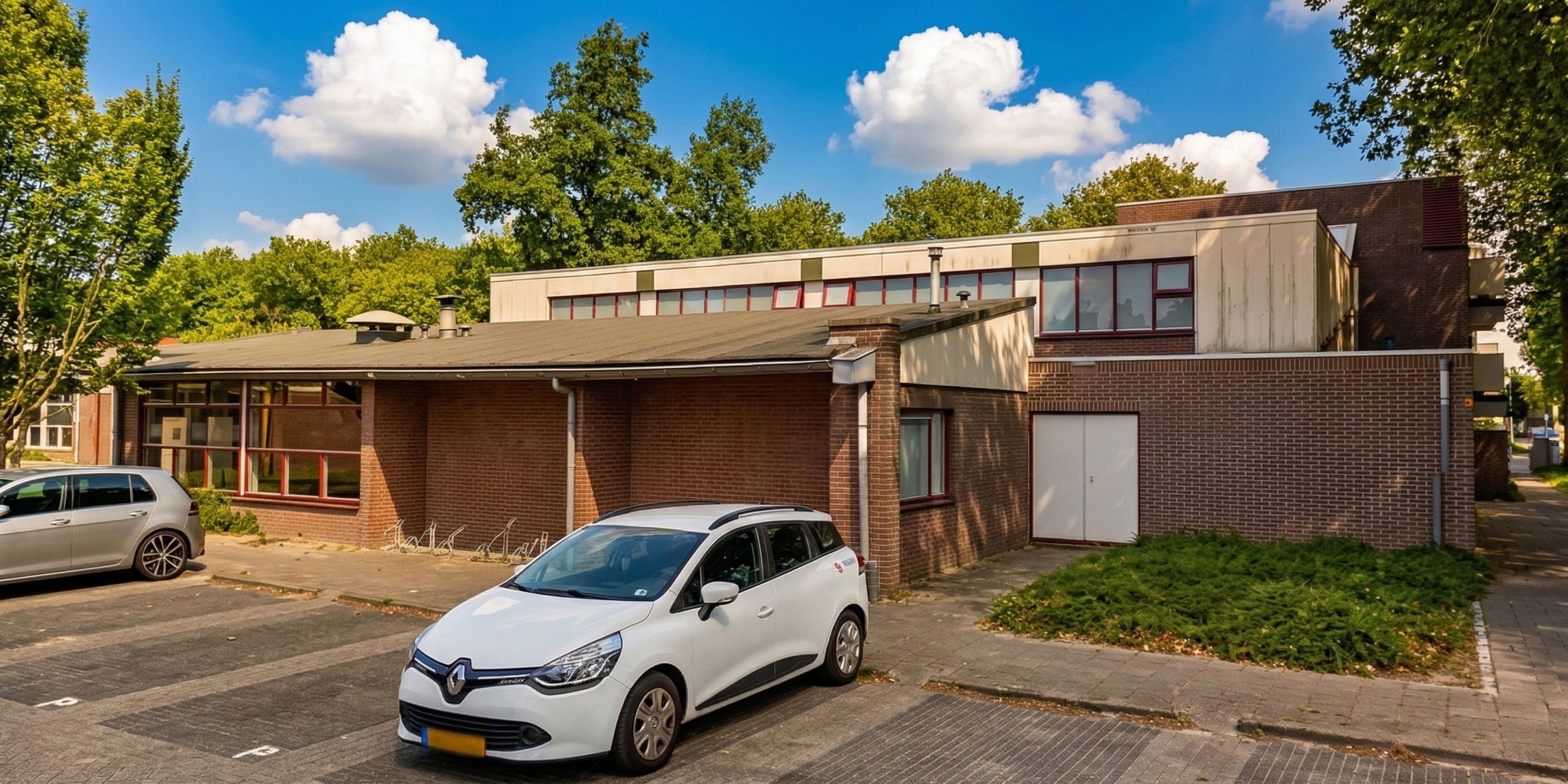 Een parkeerplaats voor een gebouw met auto’s, omgeven door bomen en een deels blauwe, deels bewolkte lucht.