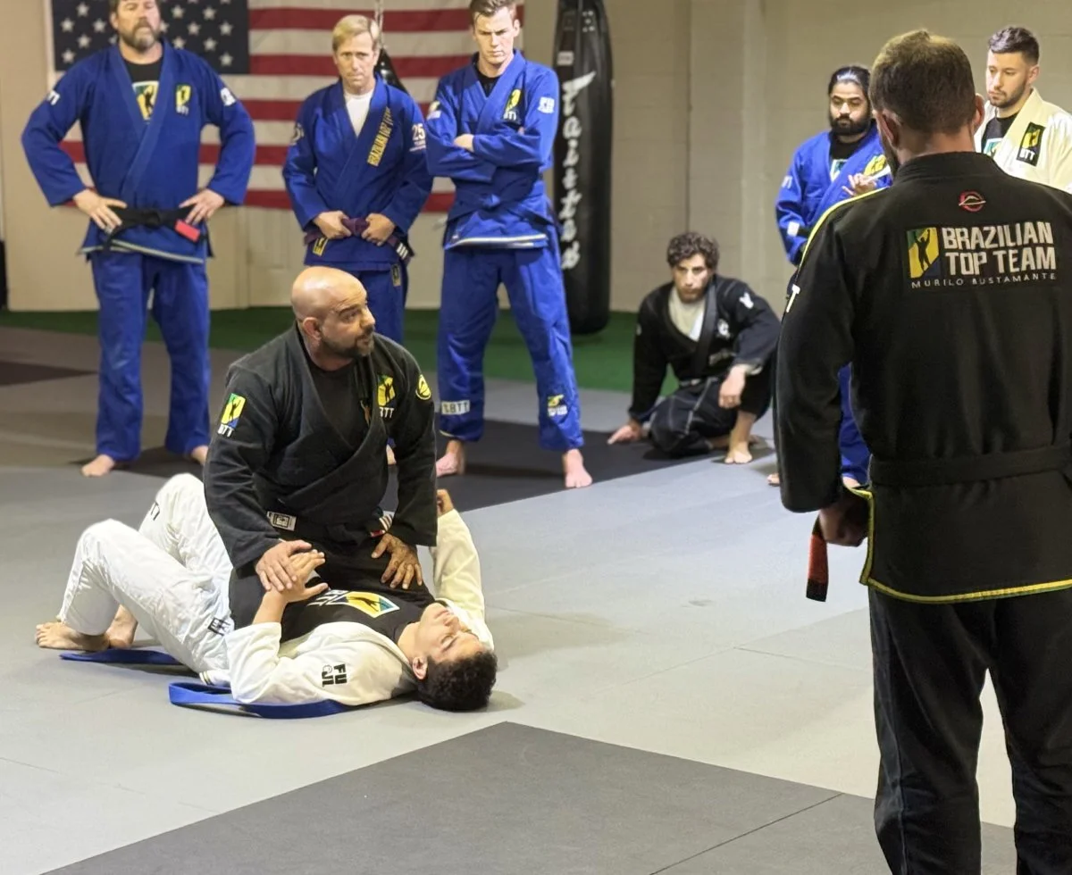 Brazilian Jiu-Jitsu instructor demonstrating a technique on a student during a class with students and instructor observing.