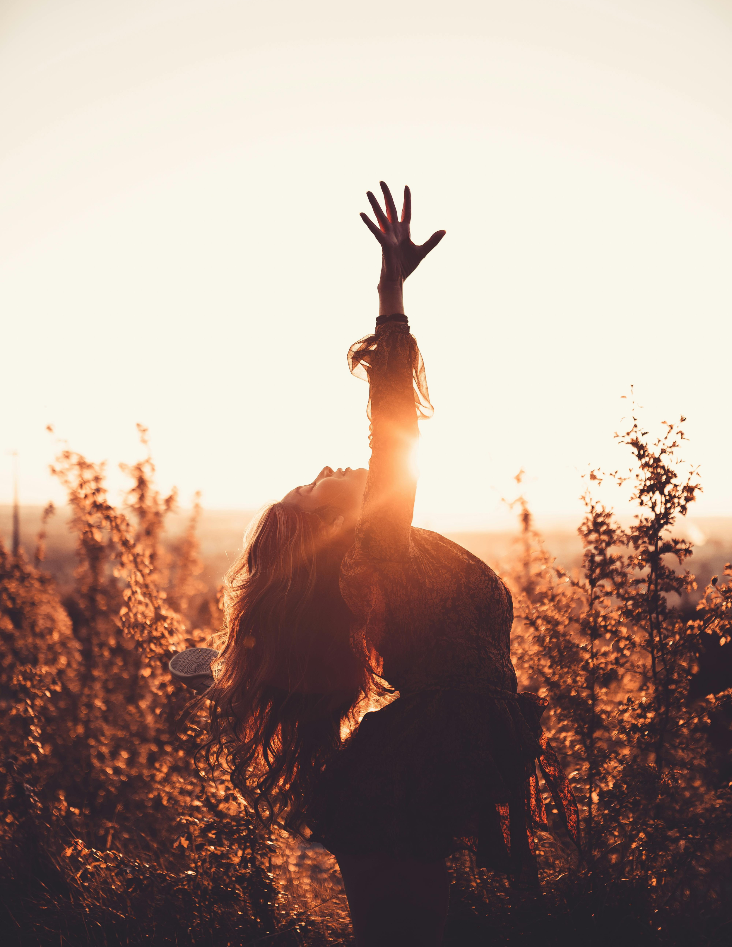 Personne levant le bras au ciel, silhouette contre un coucher de soleil, entourée de végétation. Invoque un sentiment d'union avec la Nature, de force et de bien-être.