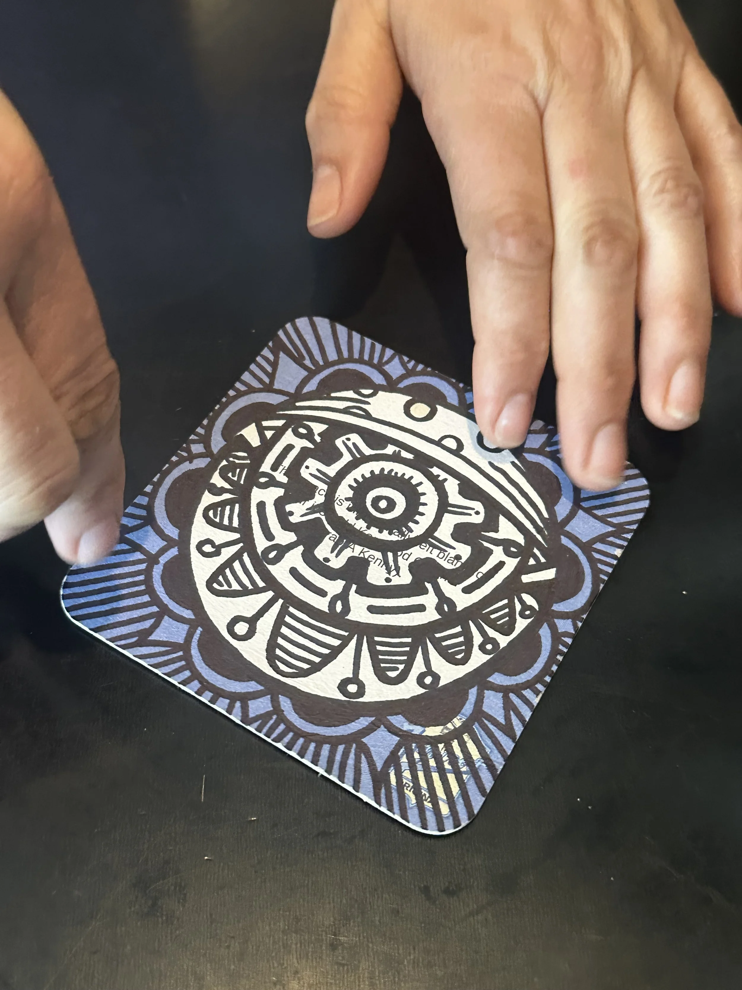Two hands holding and manipulating a colorful, illustrated card on a dark surface.
