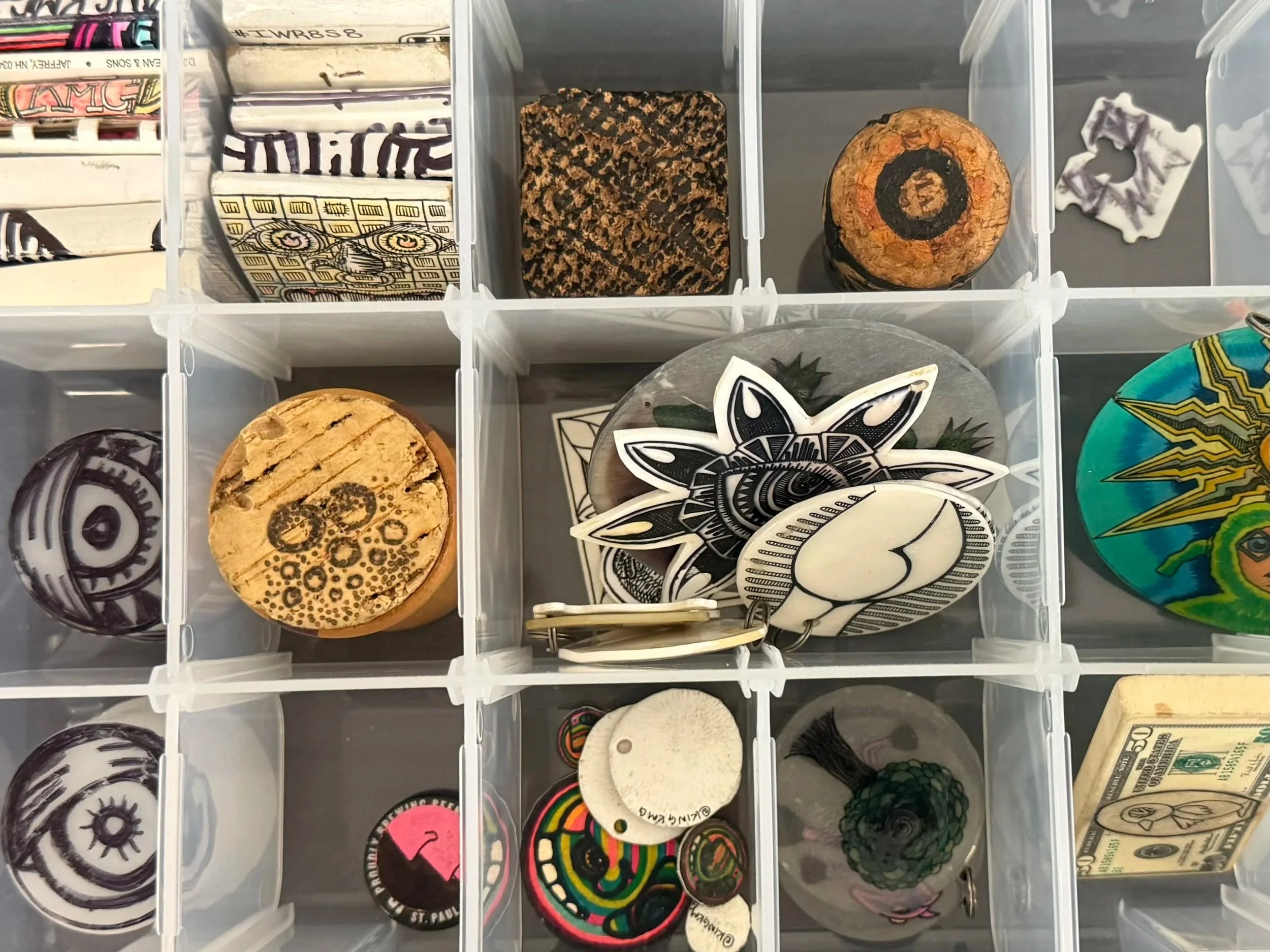 Collection of stickers, patches, buttons, and coins with various designs, stored in a transparent plastic compartment organizer.