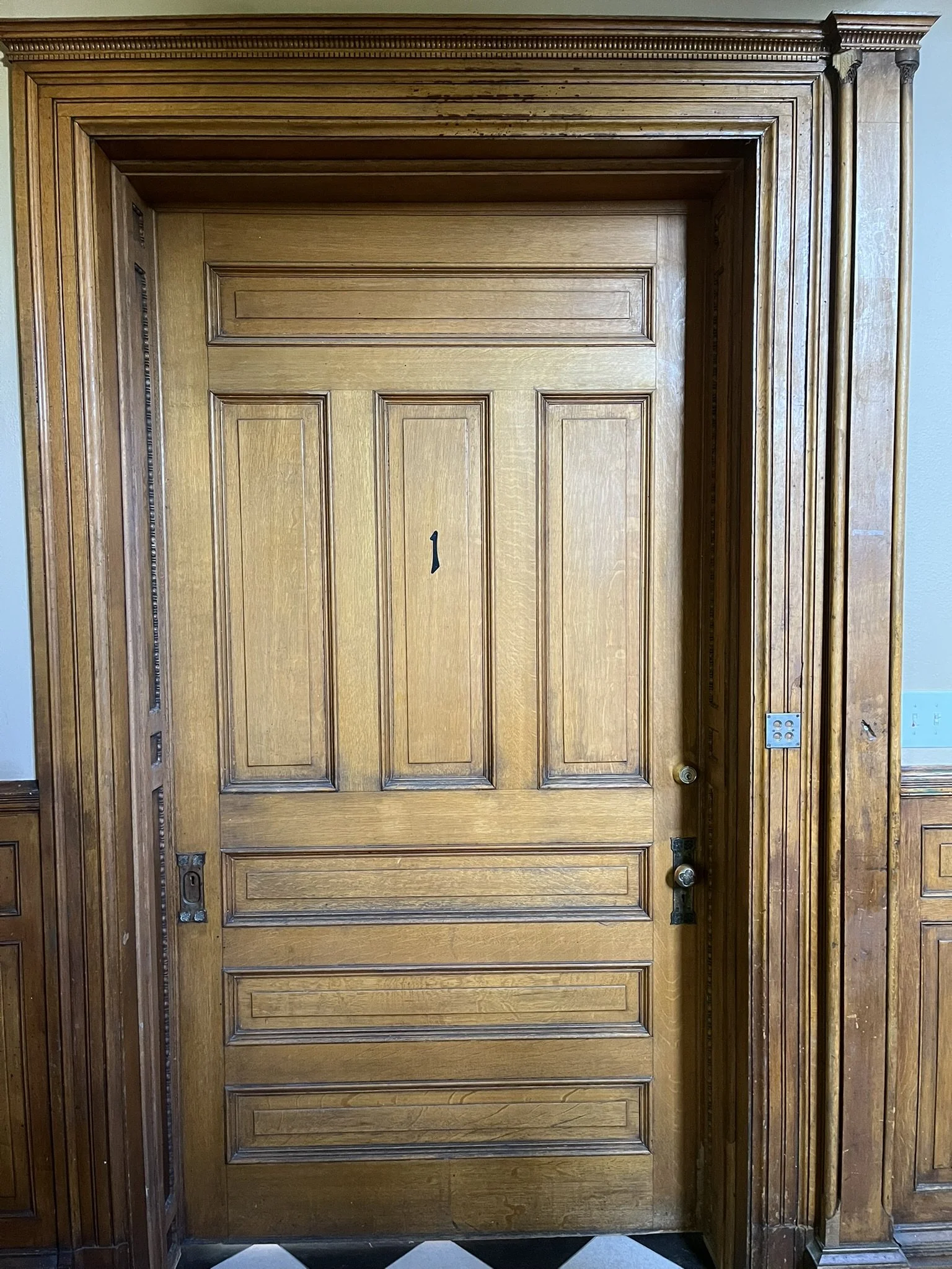 Wooden door with decorative moldings and a small gap at the bottom, surrounded by a wooden frame with detailed trim.