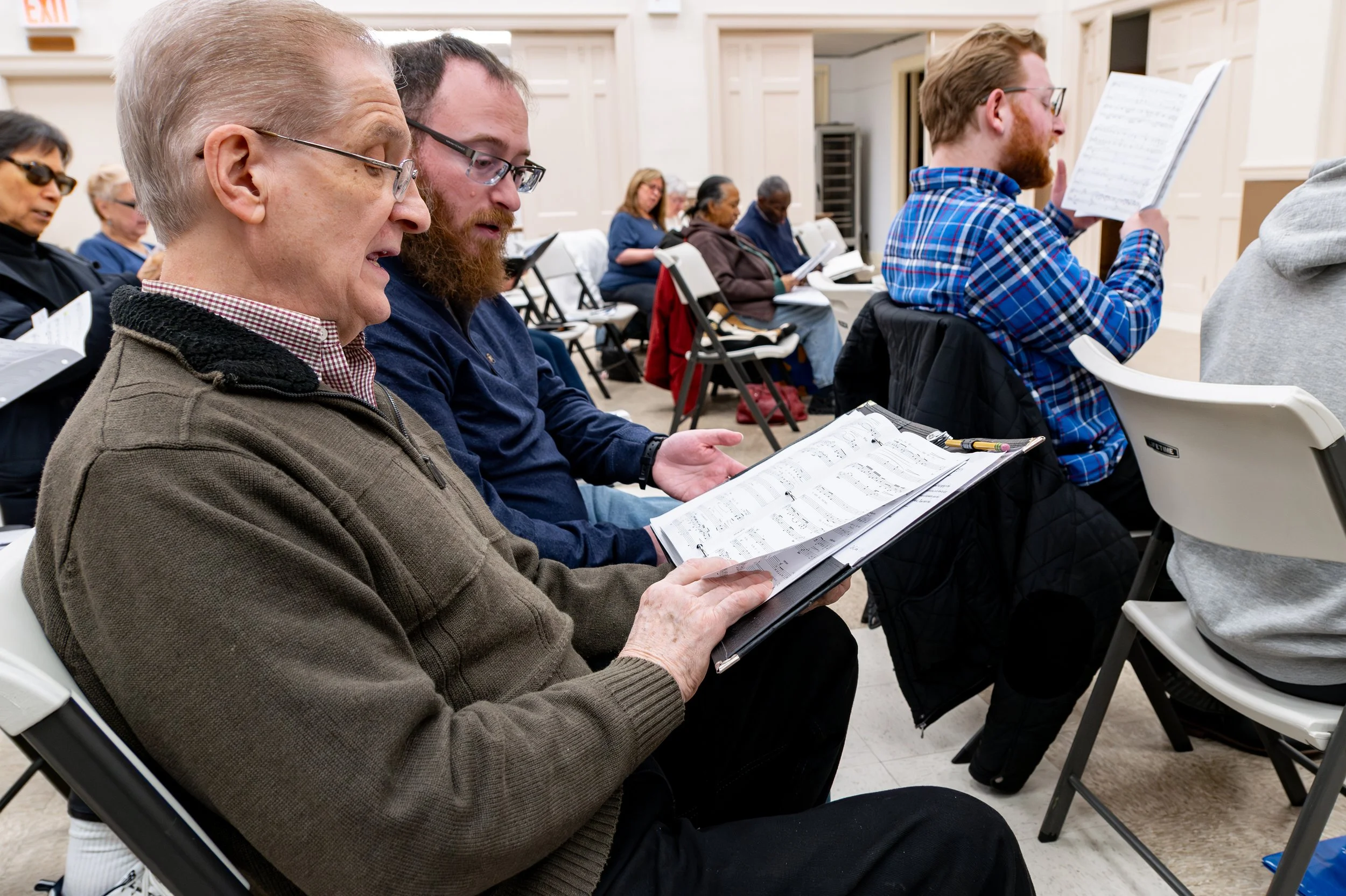Two men sharing sheet music during a Richmond Choral Society rehearsal