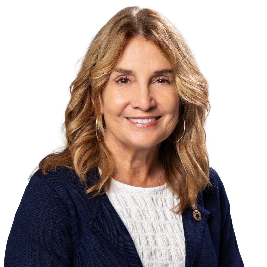 Headshot of a smiling woman with shoulder-length wavy blonde hair, wearing a navy blazer over a white textured top, and hoop earrings against a white background.