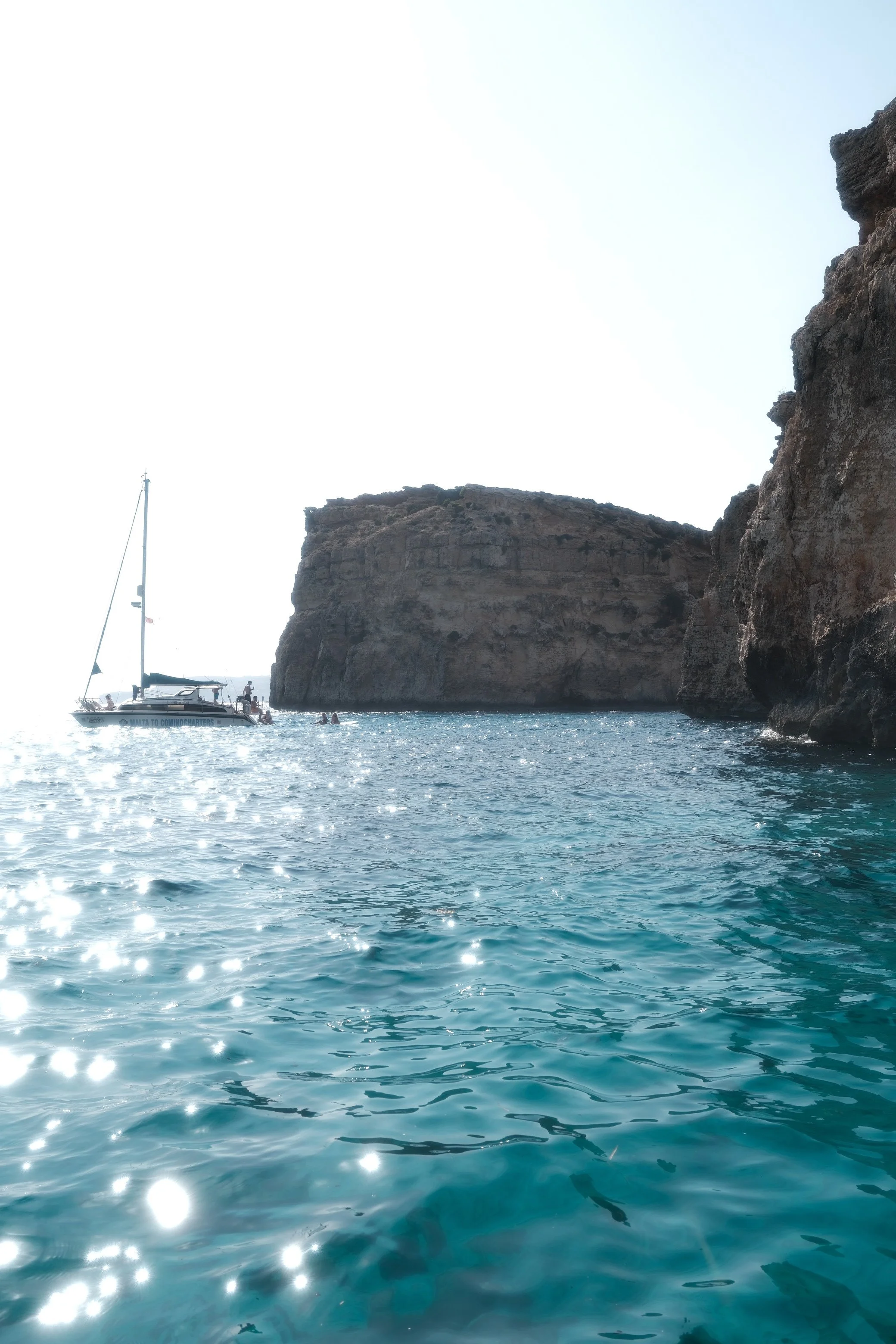 A boat sailing near rocky cliffs on a sunny day with sparkling blue water.