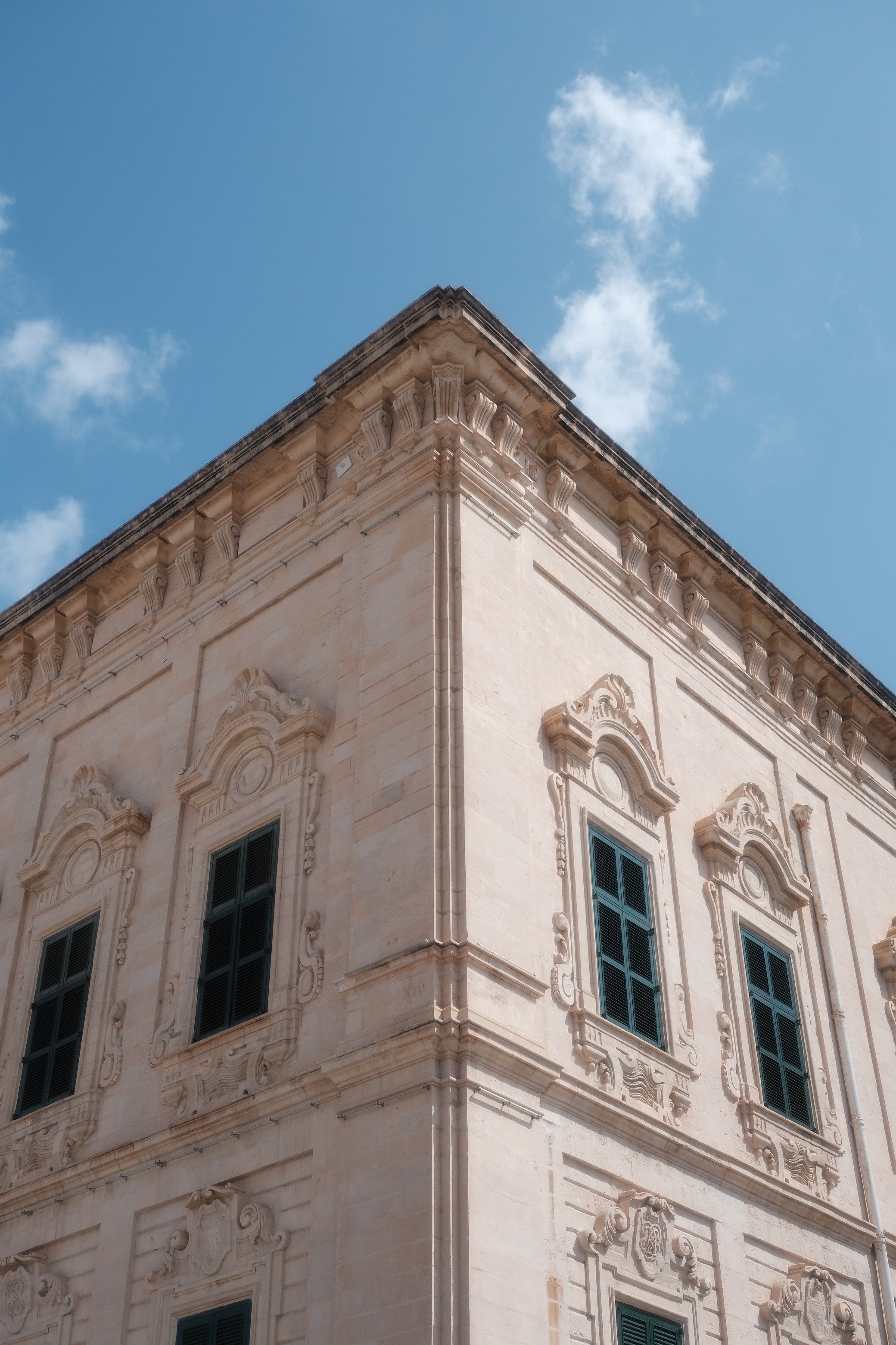 Corner of an ornate historical building with detailed architectural decorations, against a blue sky with some clouds.