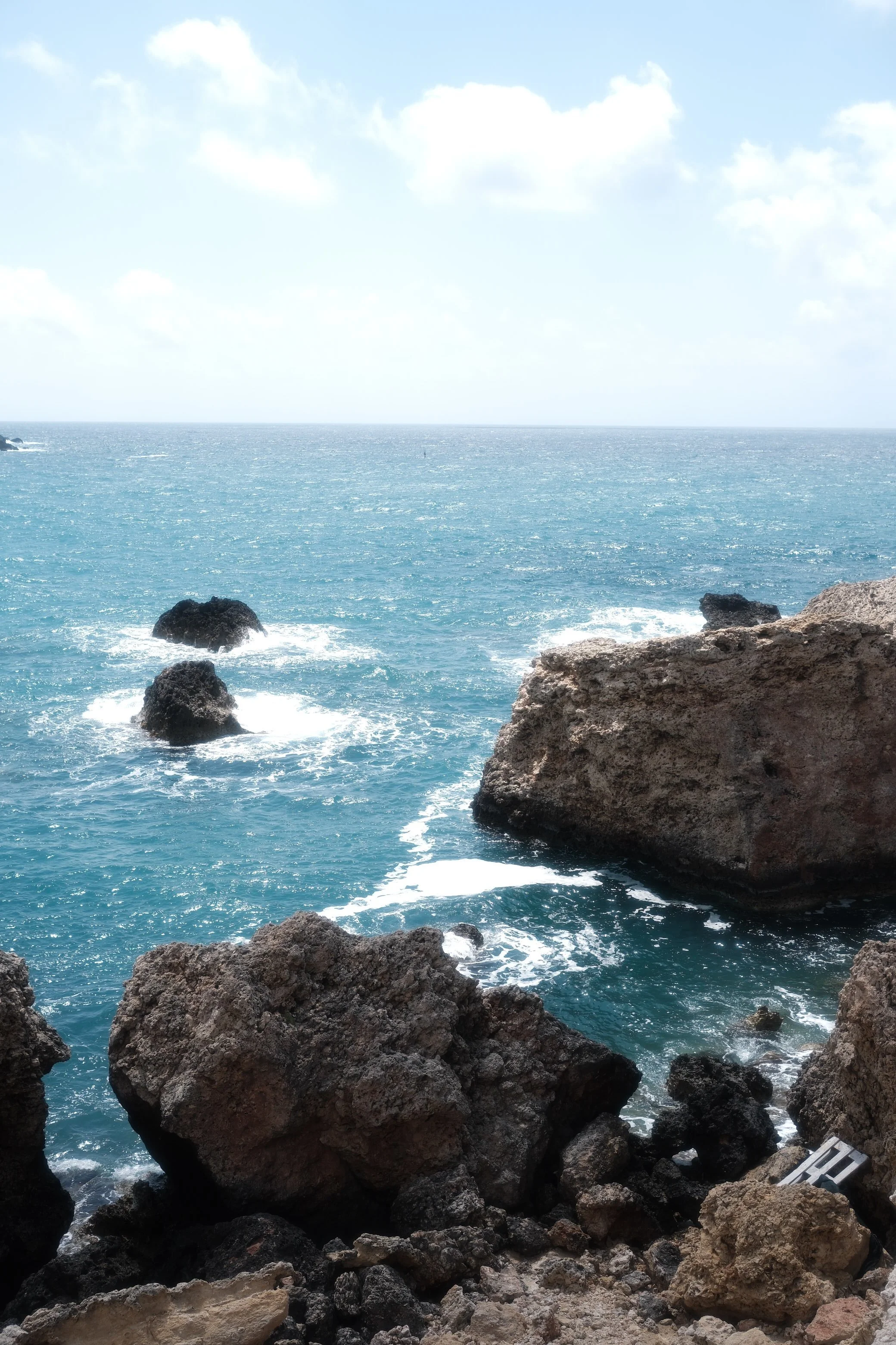 Rocky coastline with the ocean and sky in the background, scattered clouds, and gentle waves.