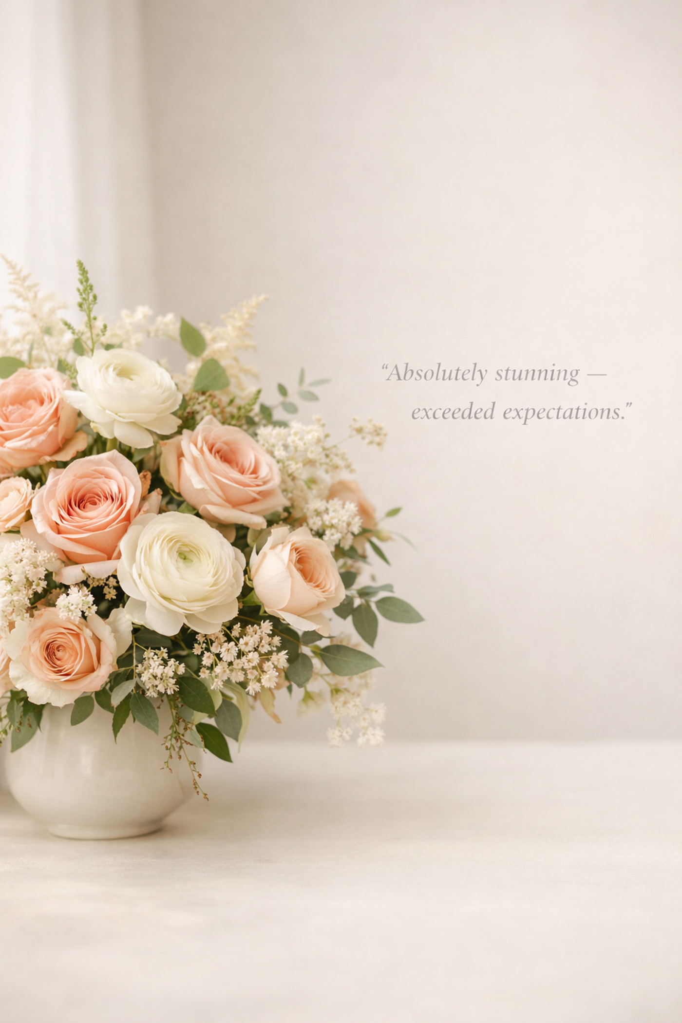 A bouquet of pink and white roses and other white flowers in a white ceramic vase, with a quote on the wall that reads, 'Absolutely stunning—exceeded expectations.'