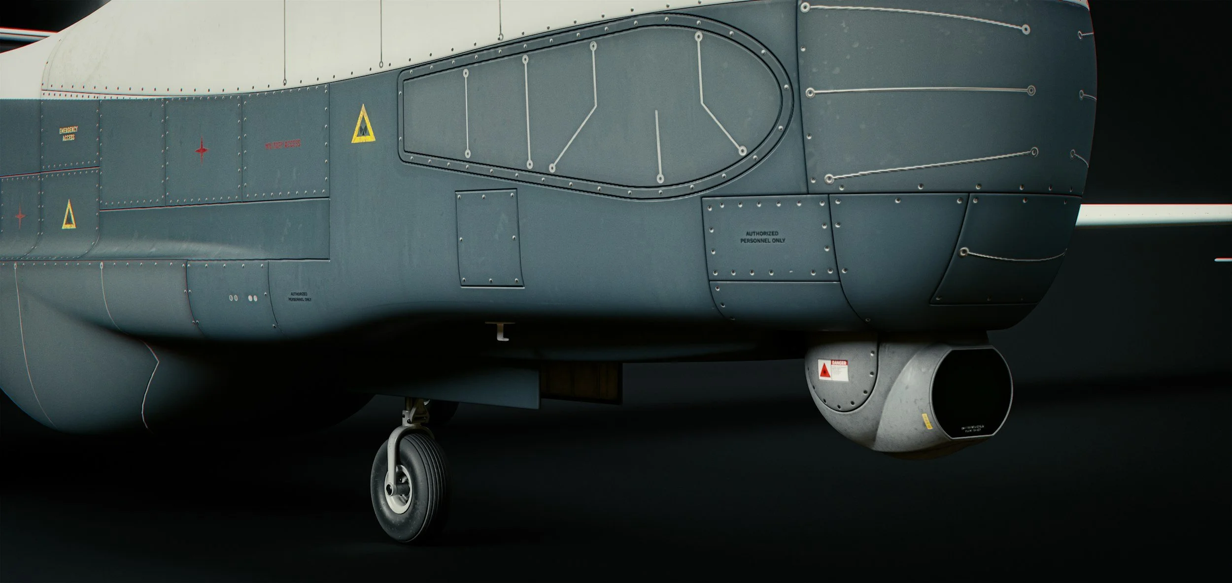 Close-up of the front section of a military fighter jet aircraft showing the cockpit area, part of the fuselage with various panels and warning labels, landing gear wheel, and a large engine exhaust at the bottom.