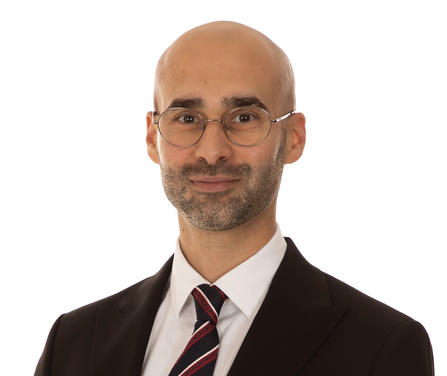 A professional man with a bald head, glasses, and a beard, wearing a white shirt, a tie with a pattern, and a black suit, against a plain background.